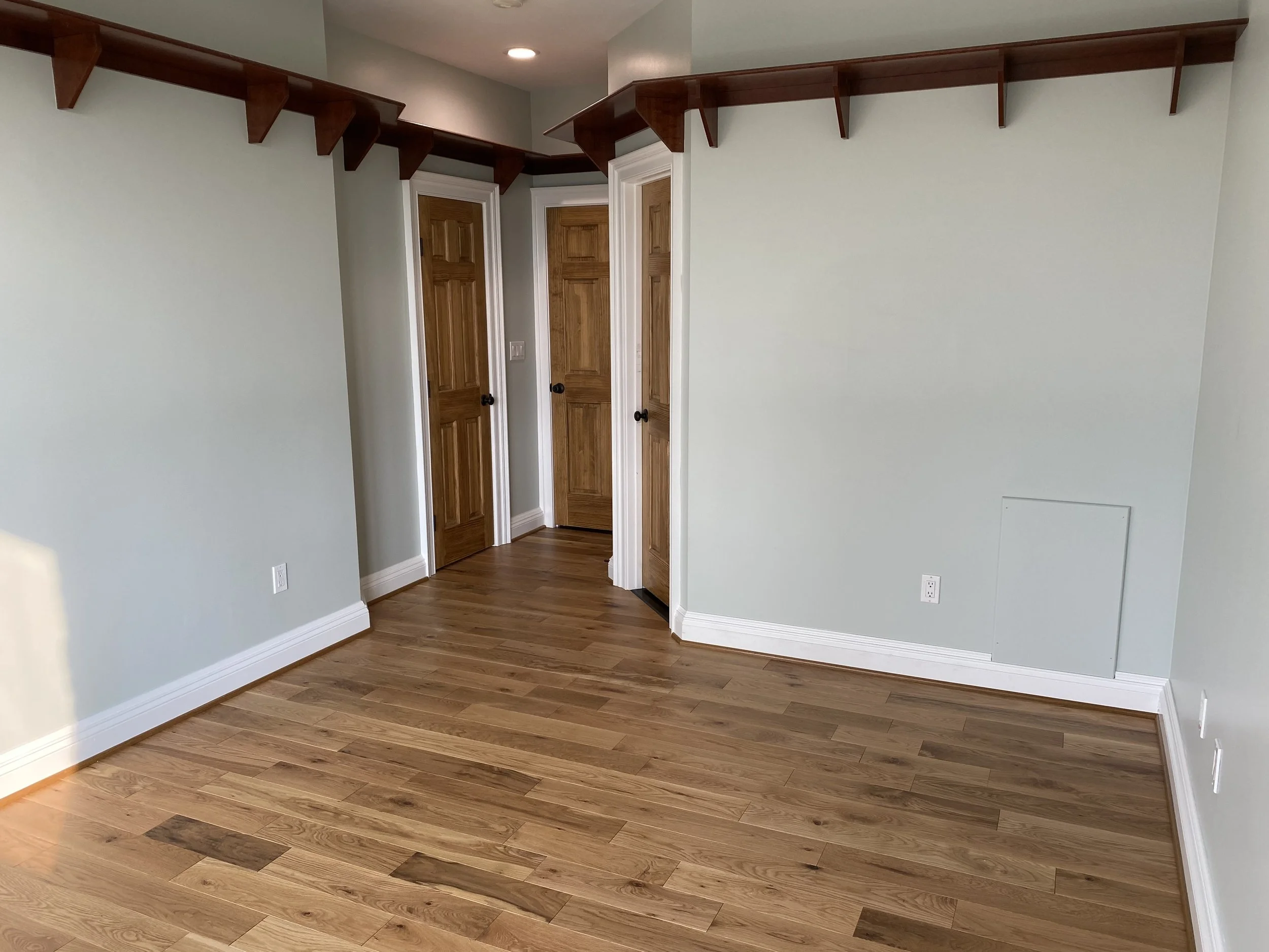 Bedroom with hardwood floors, light-colored walls, wooden doors, and wooden shelving along the ceiling.