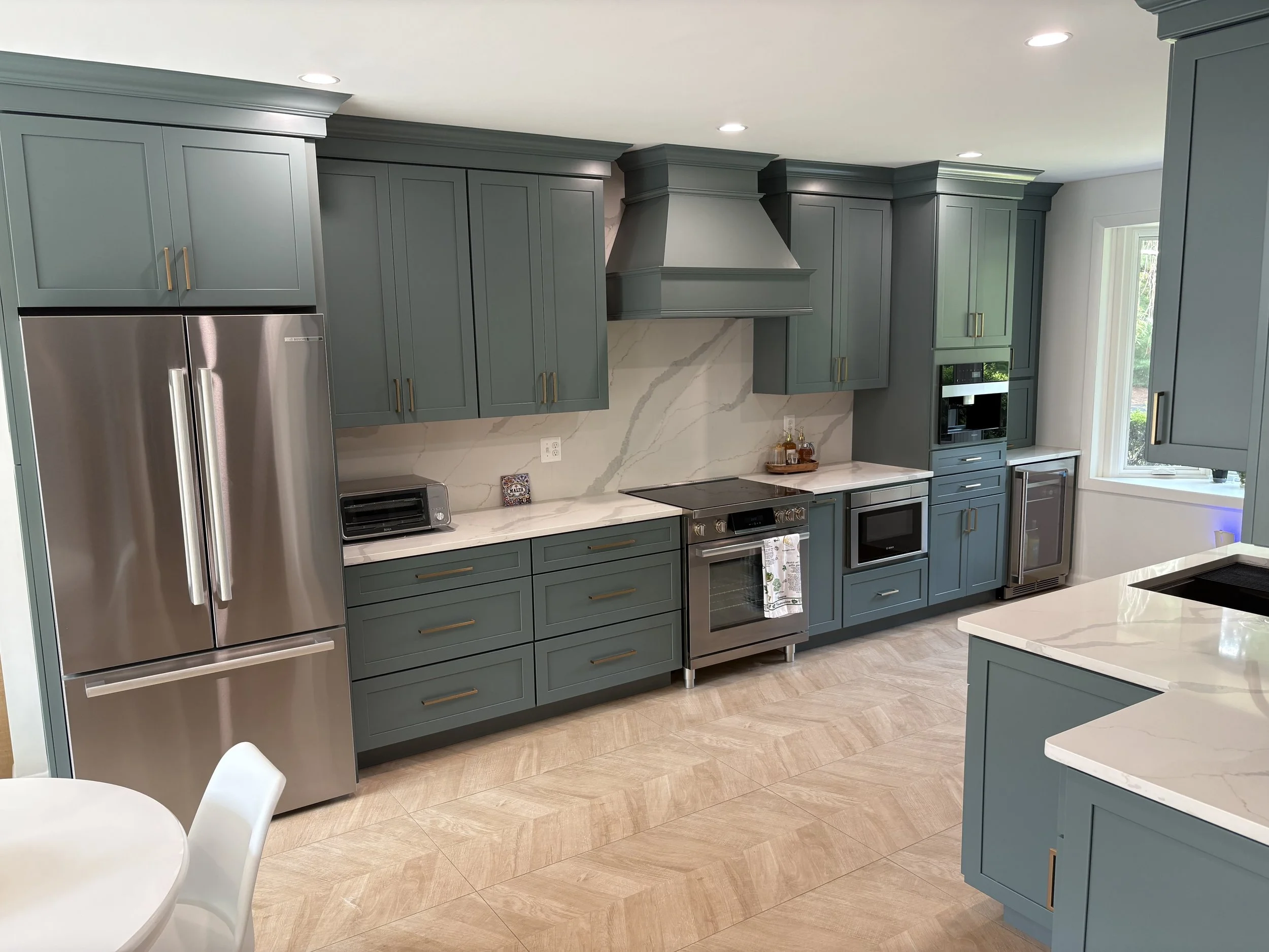 Modern kitchen with teal cabinets, stainless steel appliances, quartz backsplash, and beige 2' x4' large format tile flooring.