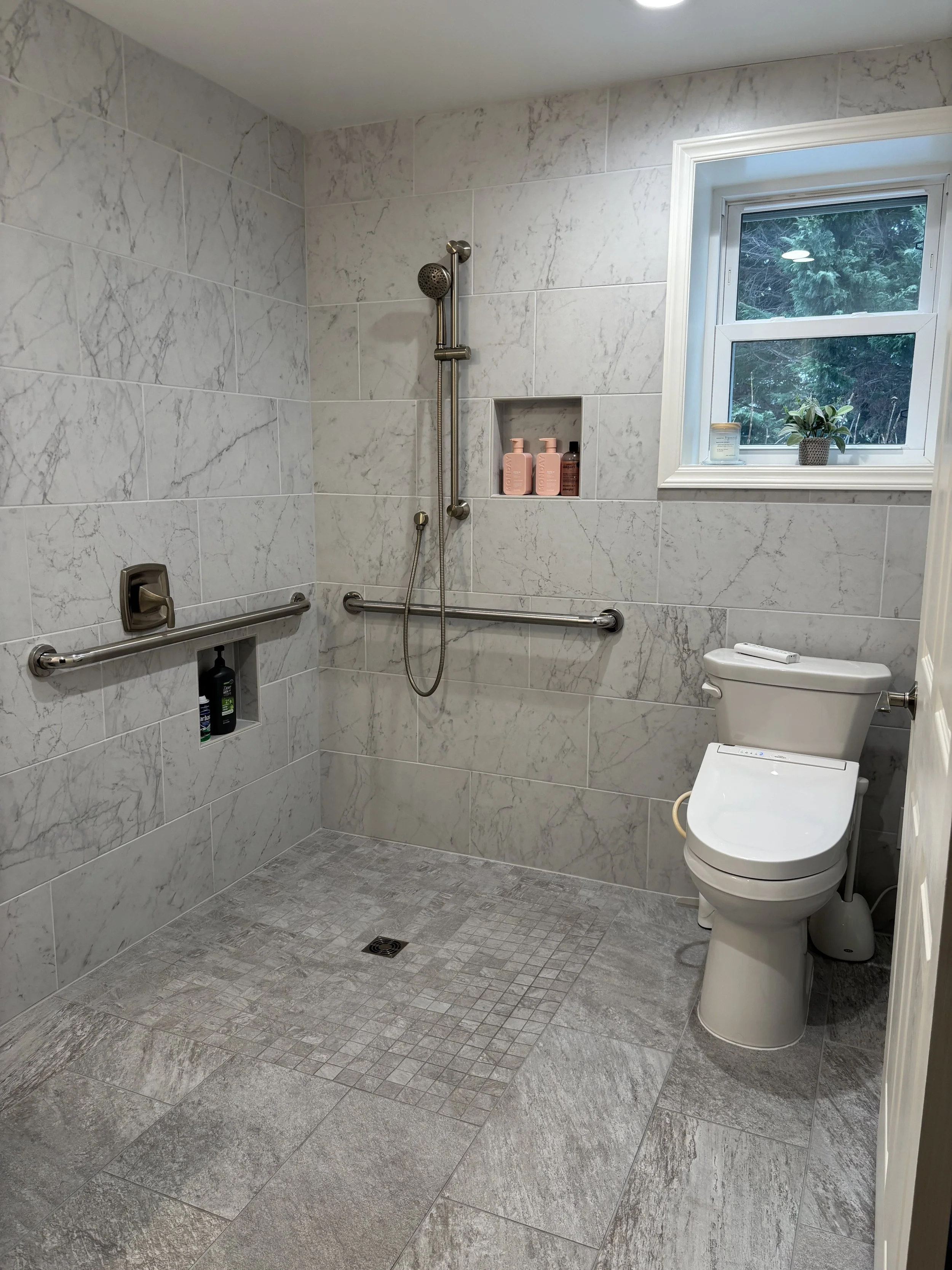 Accessible bathroom with walk-in shower, grab bars, built-in shower niche, and a toilet with bidet functions, tiled walls and floor.