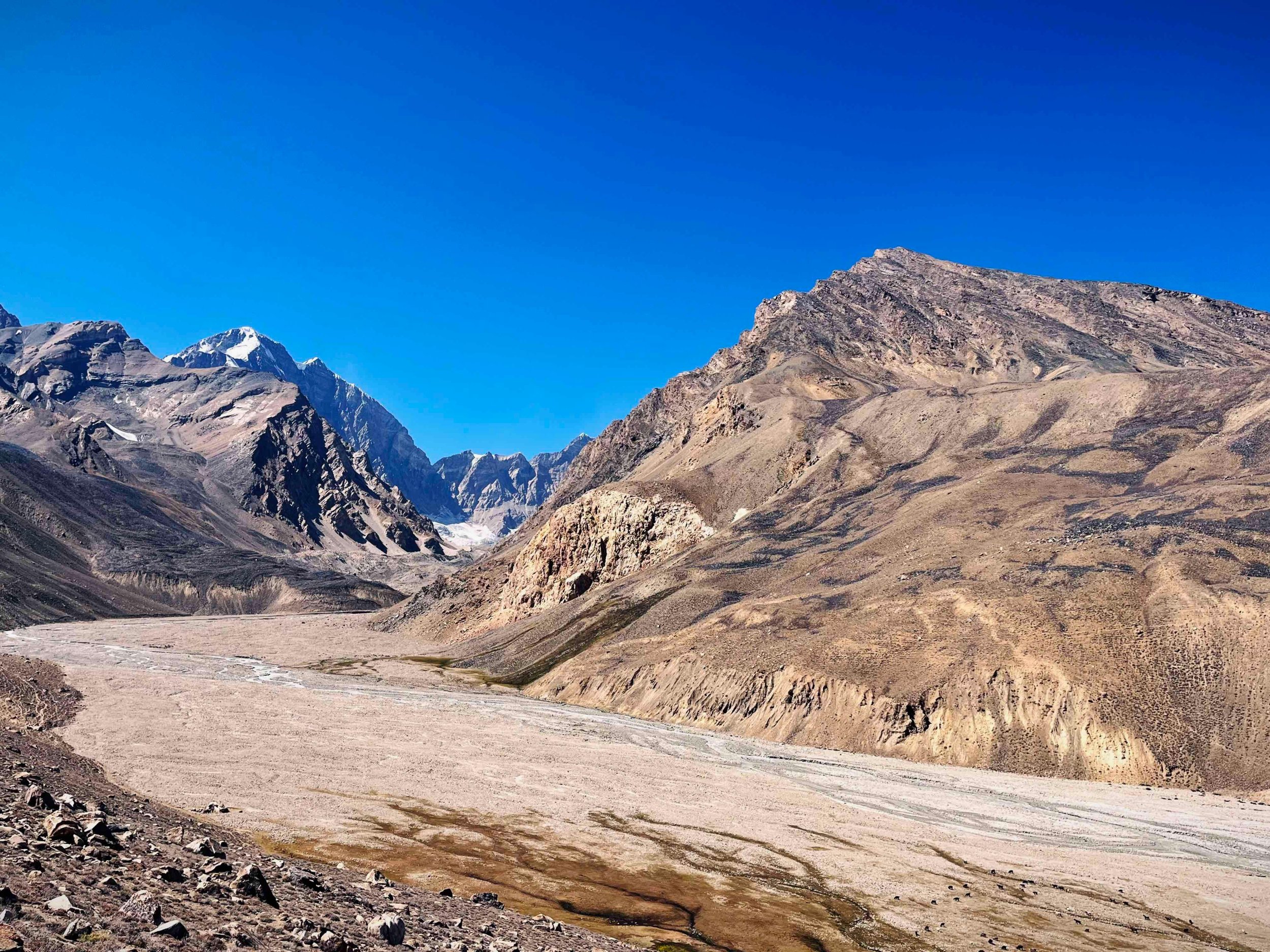 A vast mountainous landscape with brown and gray rugged hills and snow-capped peaks under a clear blue sky.