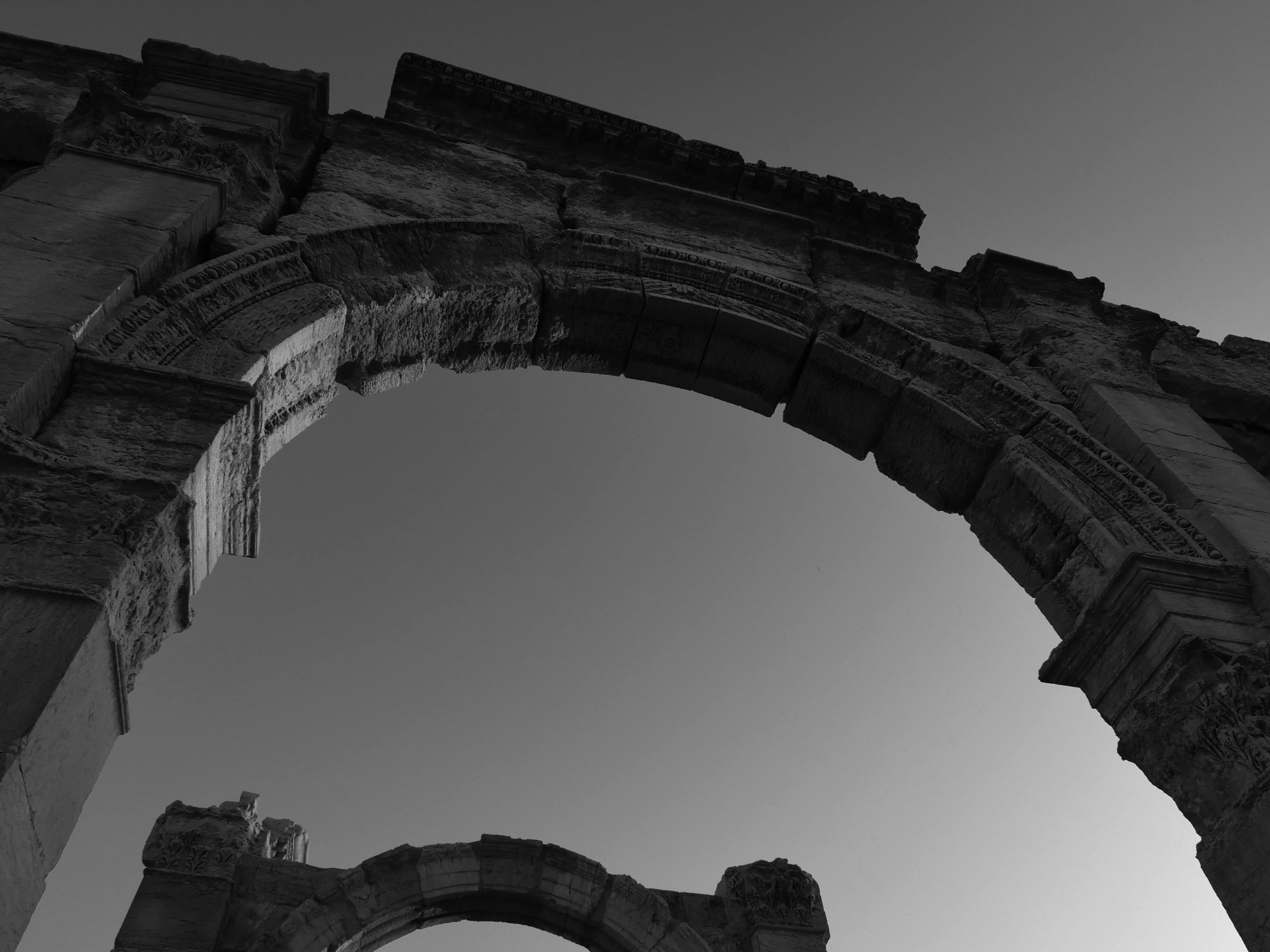 Ancient stone ruins with arches against a clear sky, black and white photo.