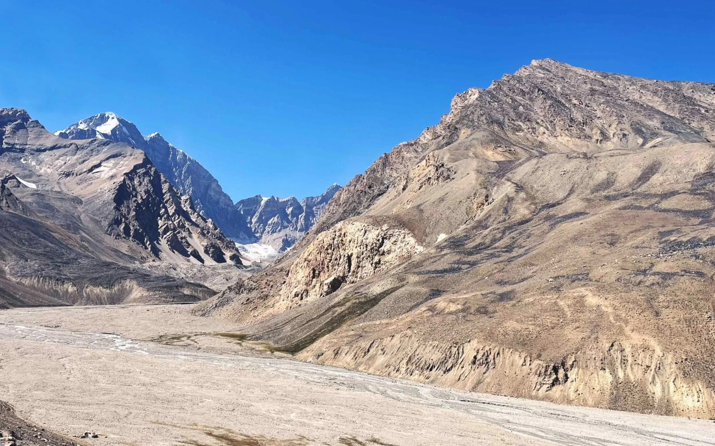 Mountain landscape in Badakhshan with rugged peaks, some snow-capped, under a clear blue sky.