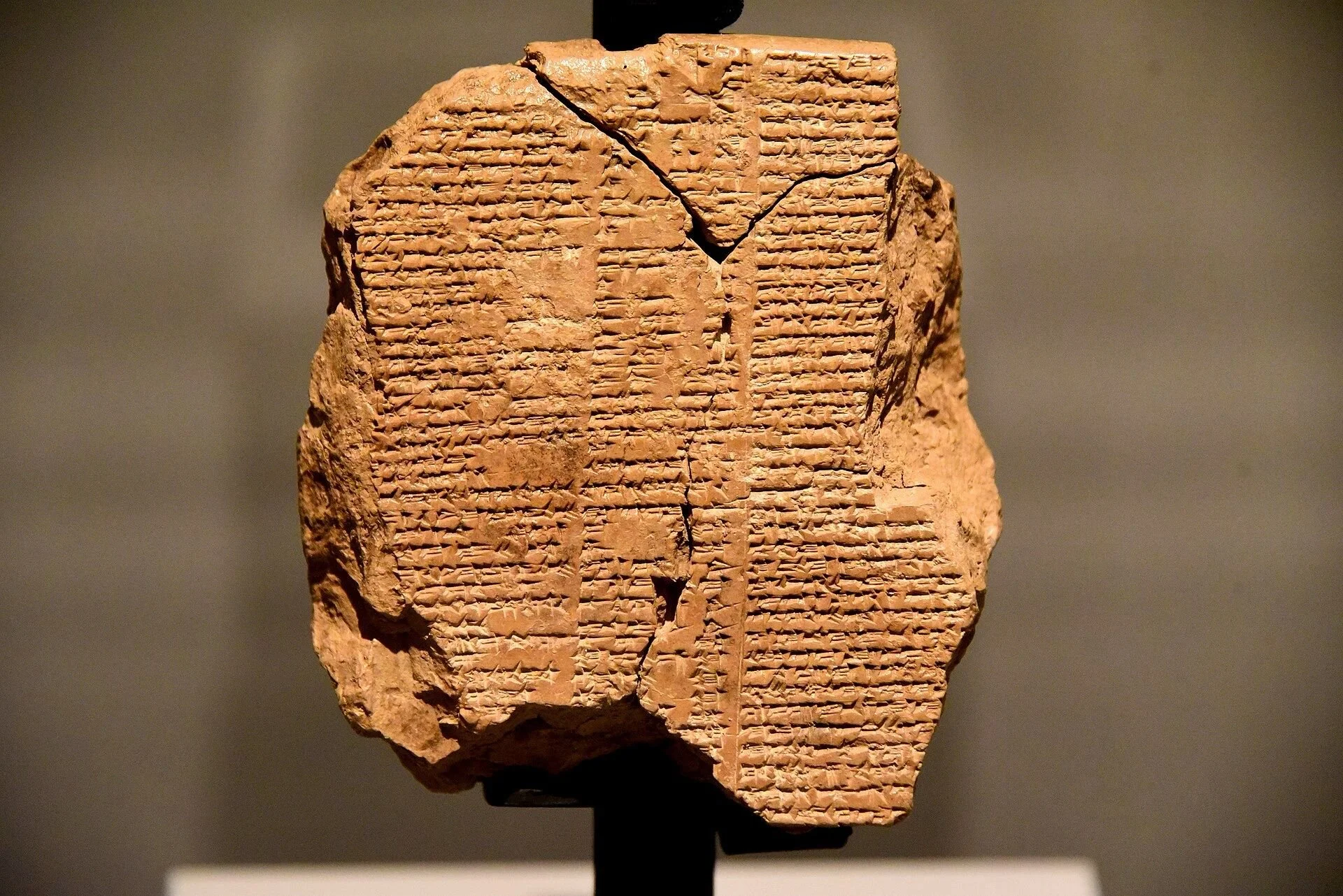 Ancient clay tablet with cuneiform writing on it, displayed on a stand in a museum.