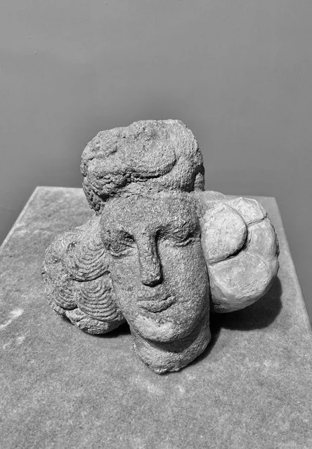 Black and white sculpture of a human face with curly hair and a large sphere on the side, displayed on a pedestal.