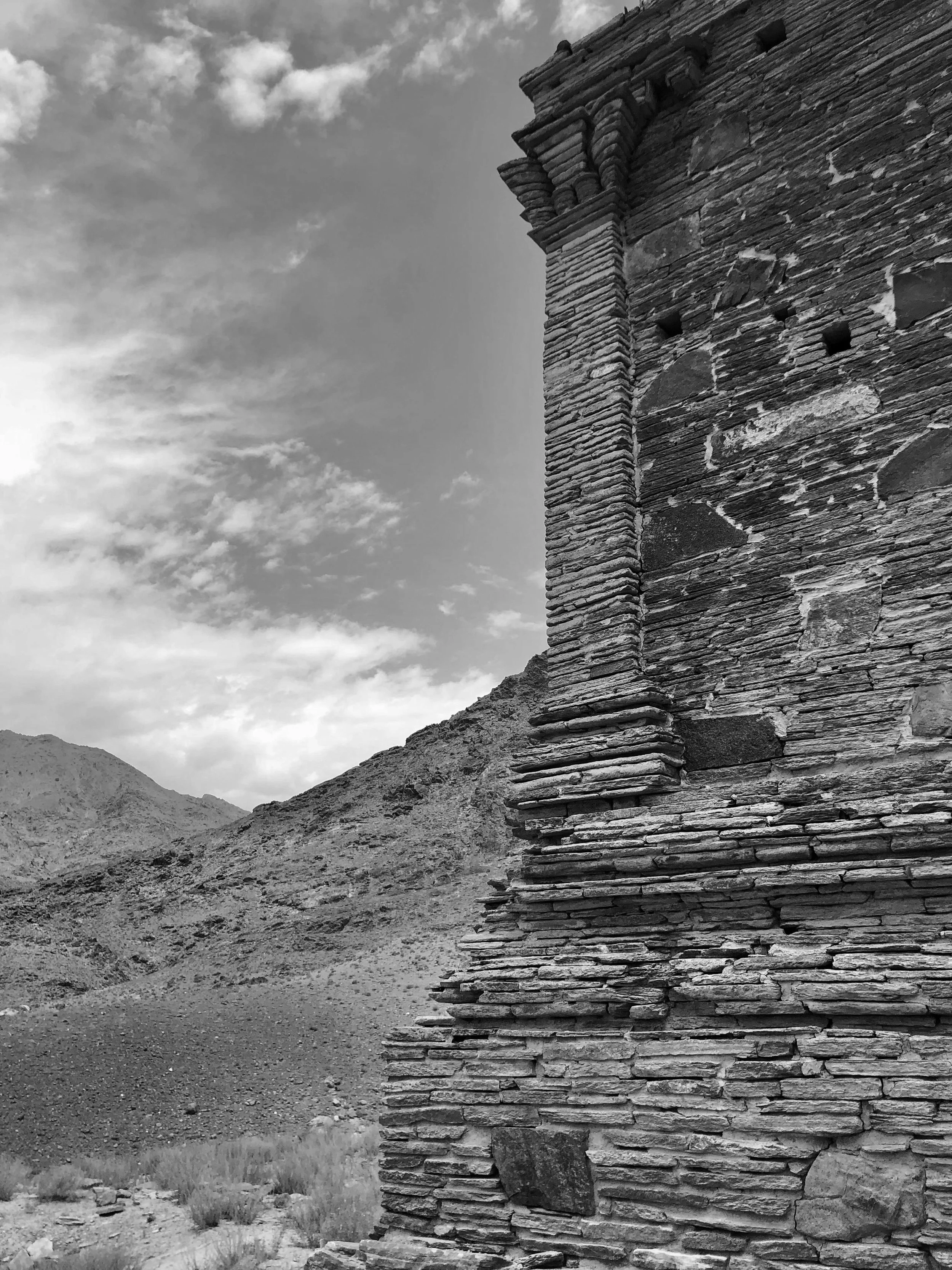 Close-up of an ancient stone building showing Greek corinthian columns craved in local stone set against a mountainous landscape and cloudy sky.