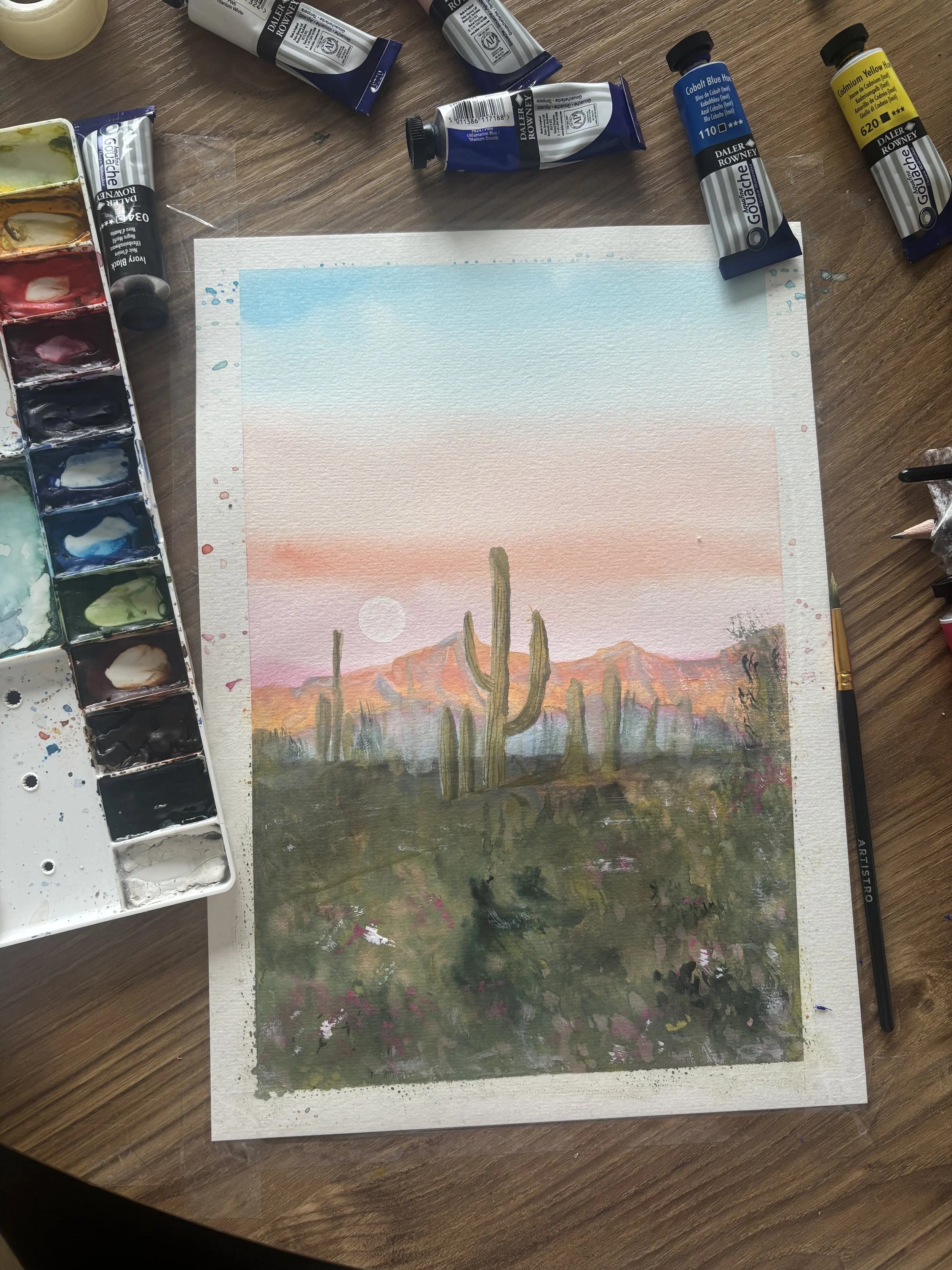 Watercolor painting of a desert landscape at sunset, featuring cacti in the foreground and mountains in the background with a pink, orange, and blue sky.