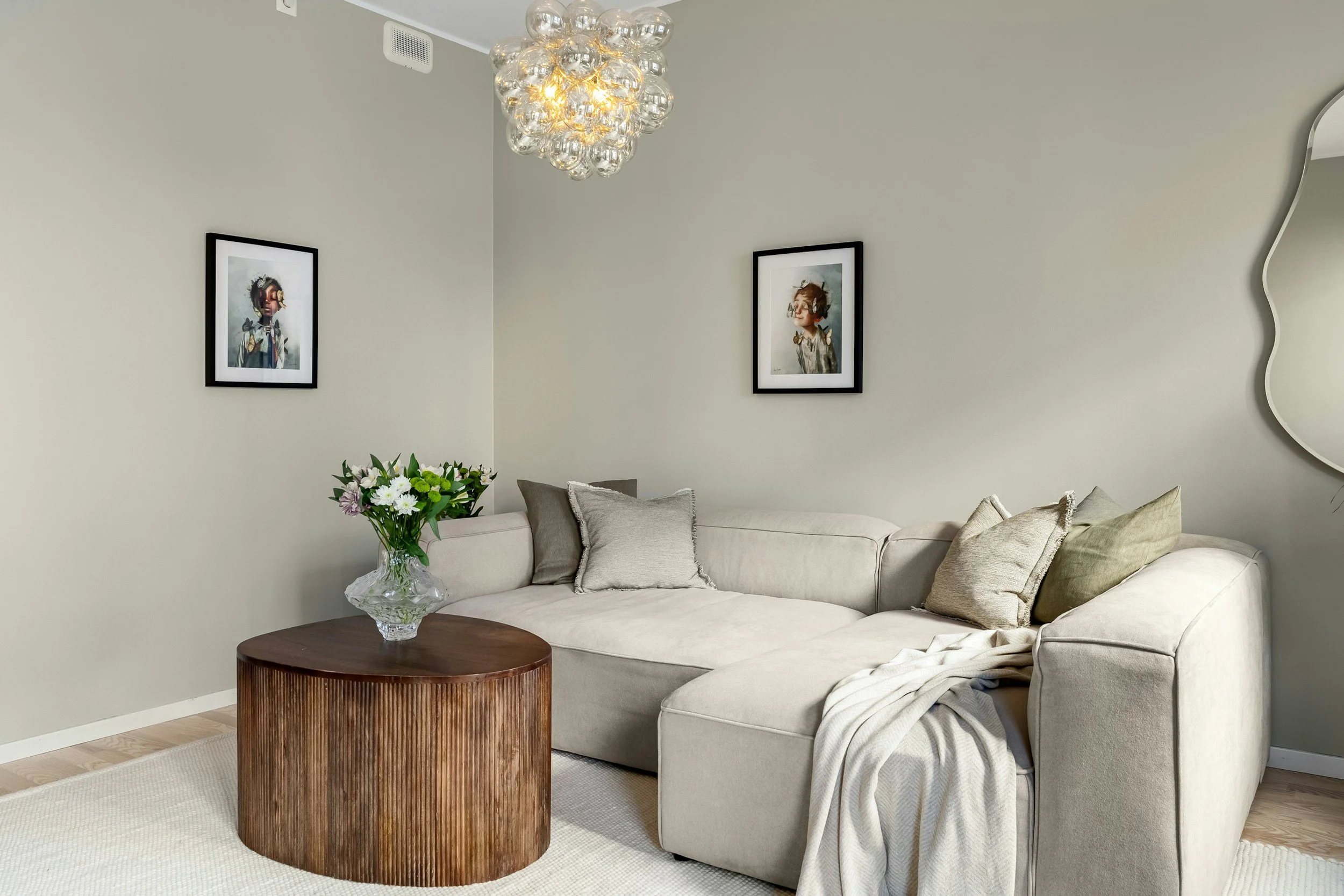 Living room with white sofa, beige pillows, wooden coffee table with glass vase of flowers, wall art, and a modern chandelier.