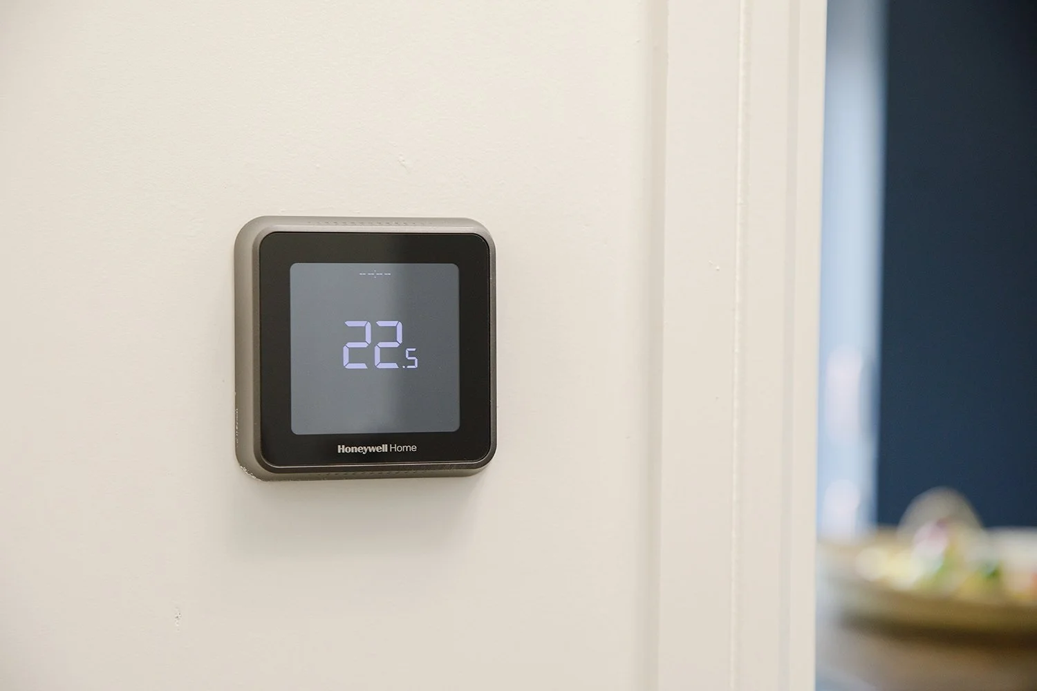 A Honeywell Home digital thermostat mounted on a white wall, displaying a temperature of 22 degrees Celsius.