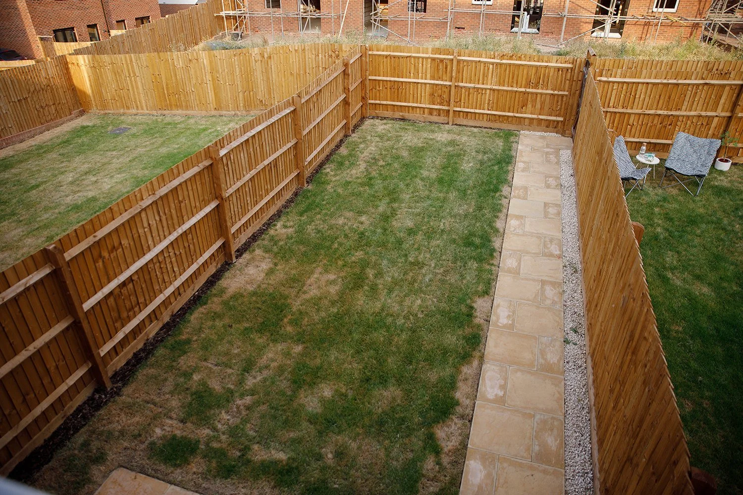 A backyard with a wooden privacy fence, a paved walkway, and a small seating area with two chairs and a table.