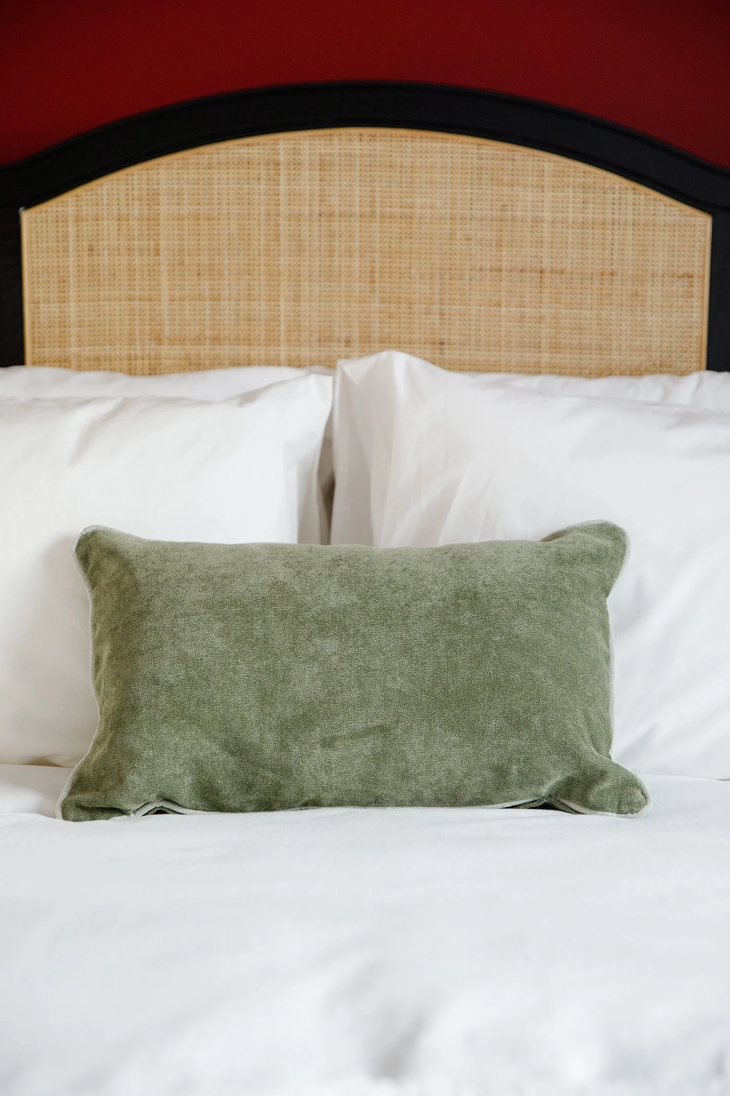 A bed with white sheets, a green pillow, and a beige headboard with a black border, set against a red wall.