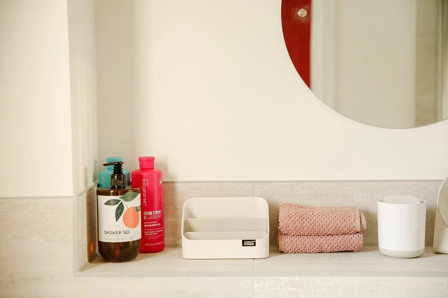 Bathroom shelf with soap dispenser, shampoo bottles, a white container, pink towels, and a white cup.