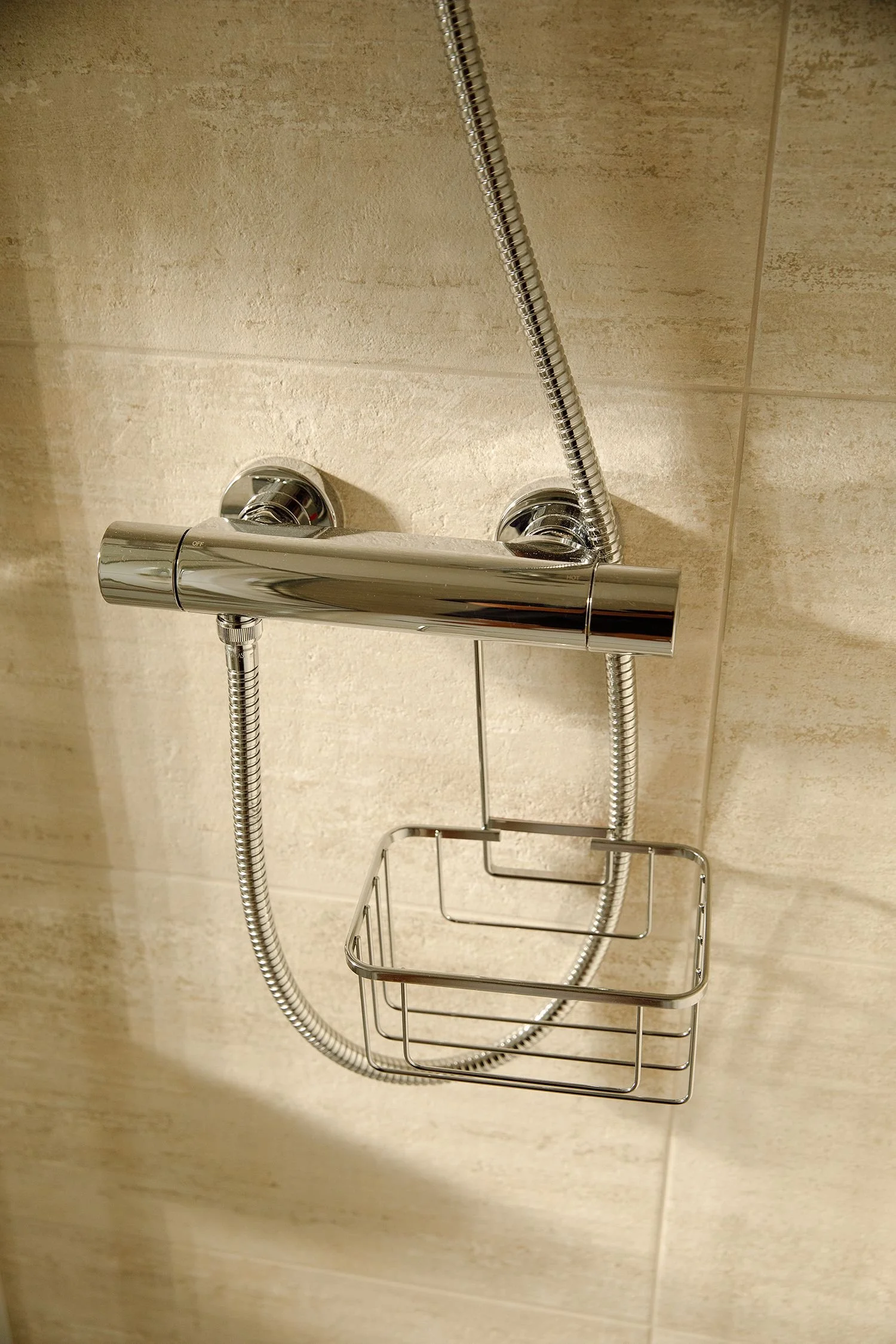 Shower fixture with a chrome finish, including a horizontal shower bar, a shower head, a flexible shower hose, and a wire shower caddy hanging below.