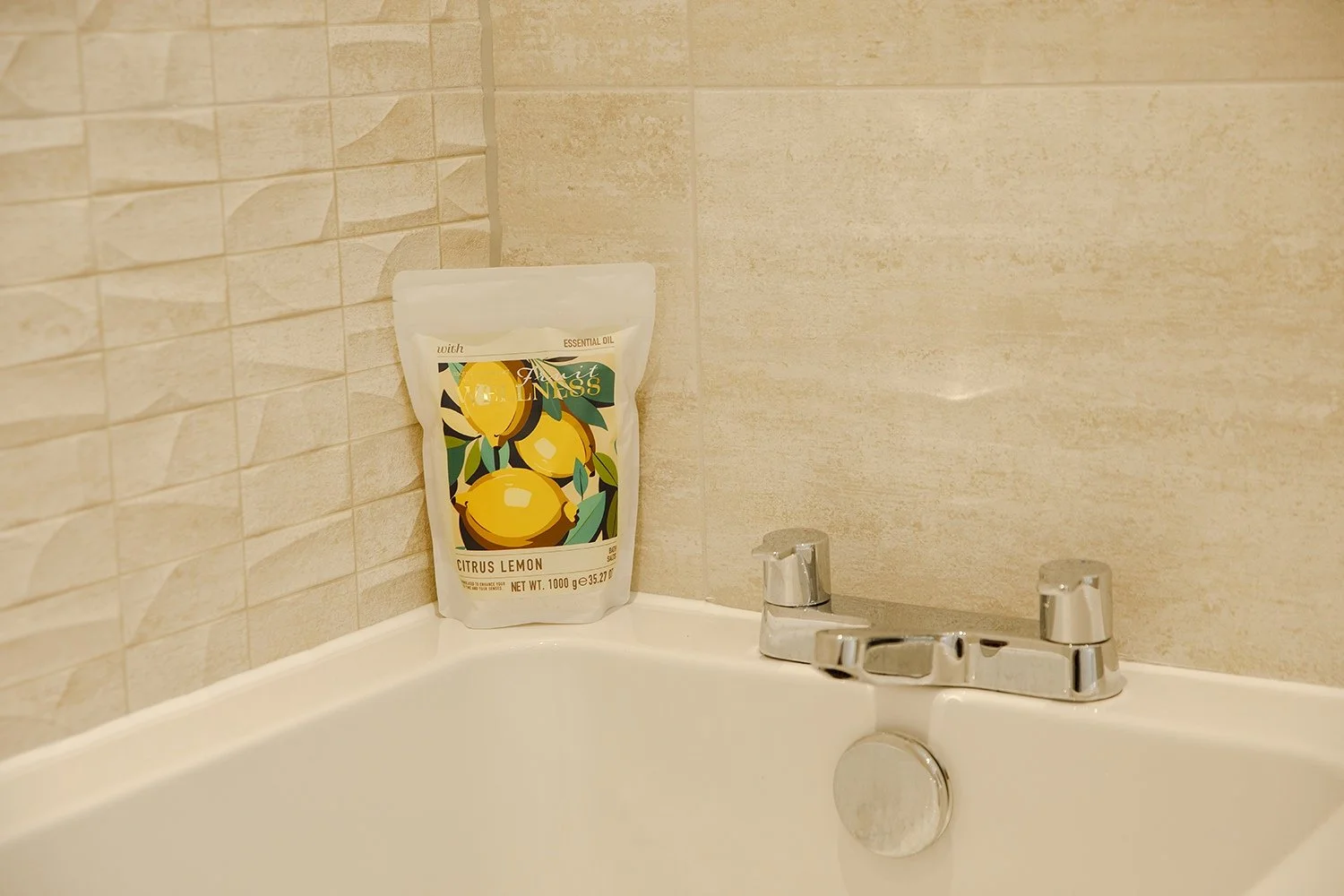 A bathroom corner showing a white bathtub, a silver faucet, and a bag of citrus lemon essential oil on the bathtub edge.