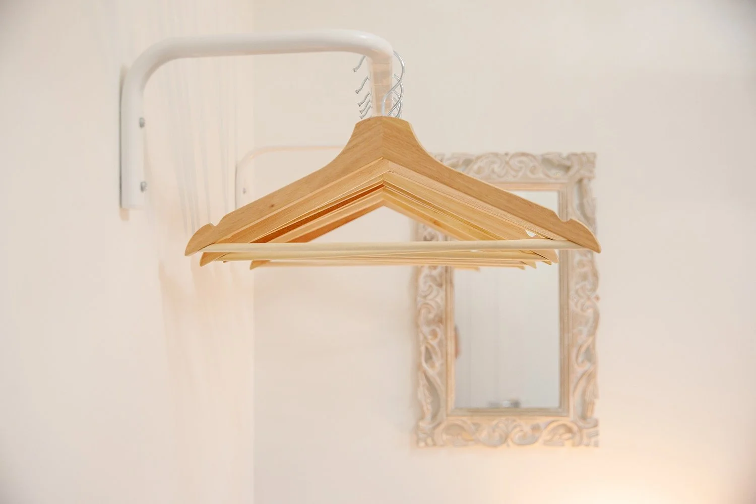 Several wooden hangers hanging from a white wall-mounted rack, with a decorative mirror in the background.