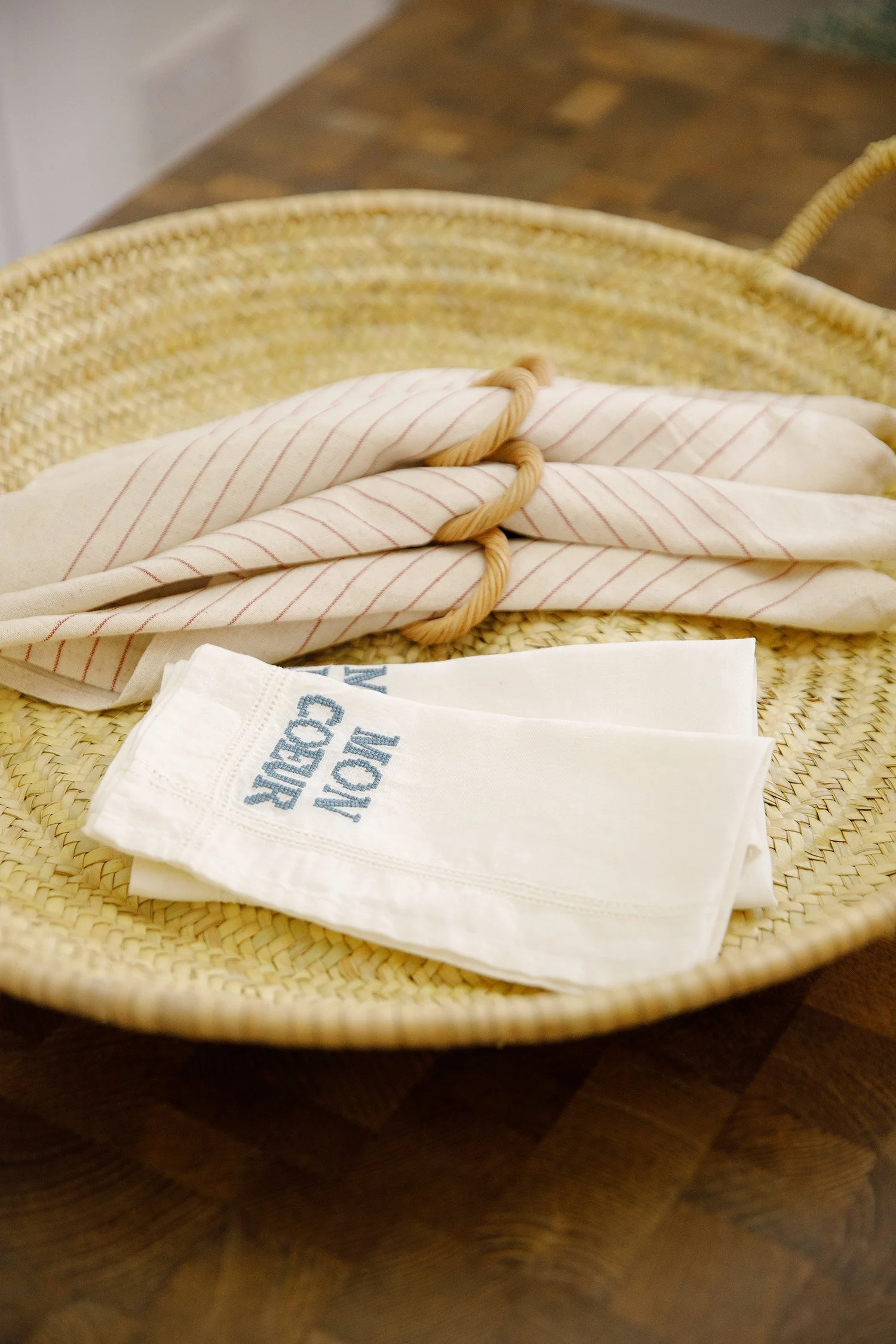 A woven basket with cloth napkins and a cloth towel inside, placed on a wooden table.