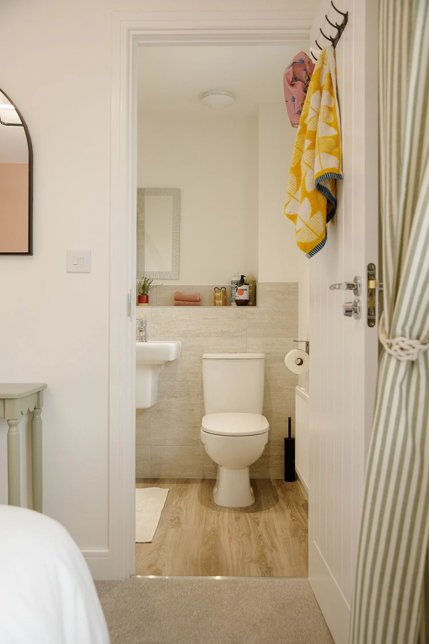 Bathroom with white toilet, small sink, mirror, and decorative towels hanging on a hook on the door.