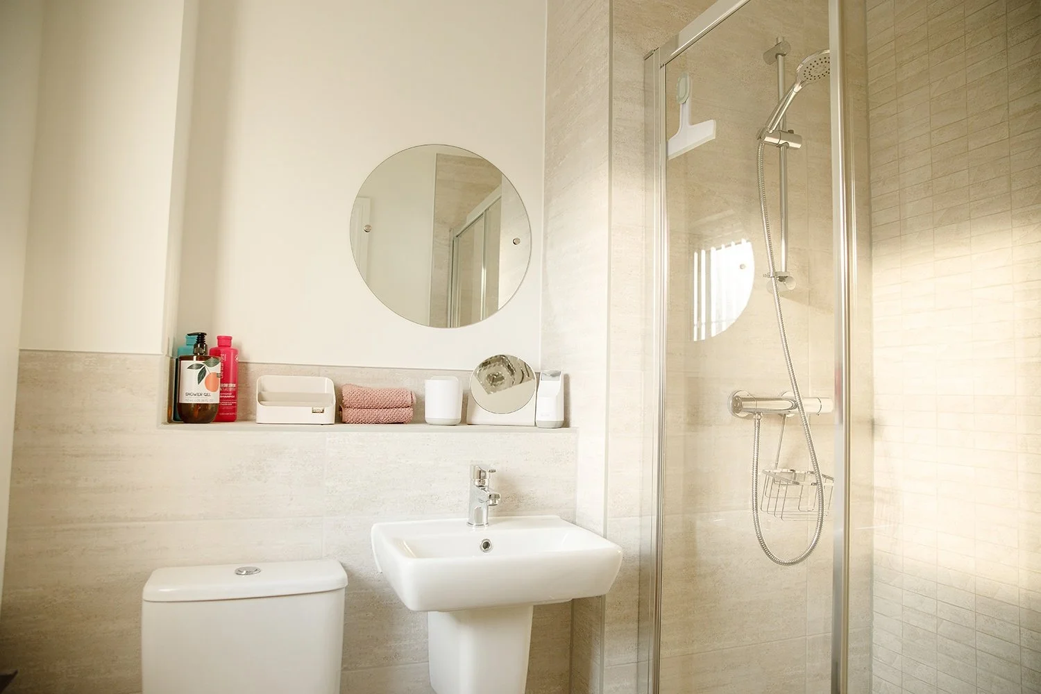 Bathroom with a white toilet, a white sink, a mirror, and a glass shower with a handheld showerhead.