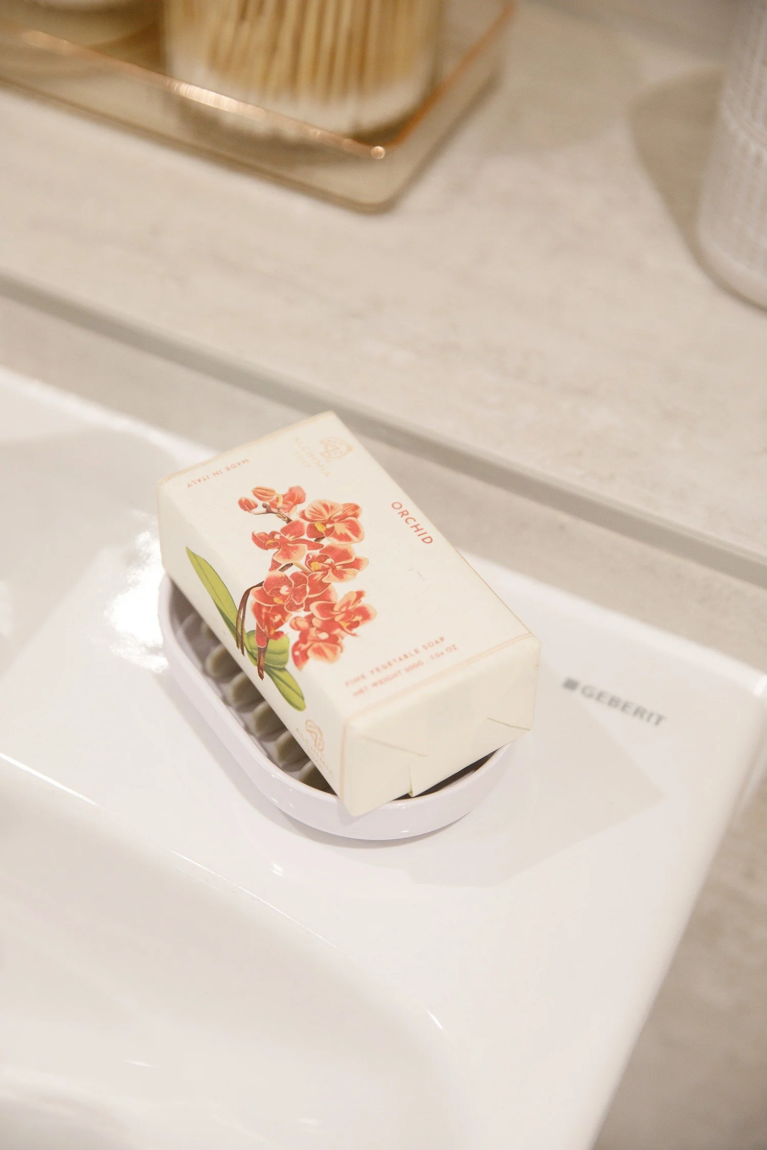 A box of orange orchid scented vegetable soap on a white bathroom sink.