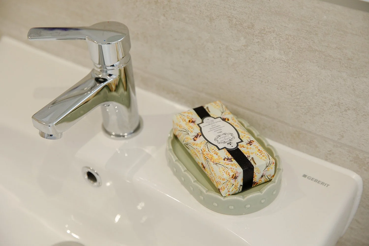 A bathroom sink with a chrome faucet and a soap dish holding a wrapped bar of soap with floral and bee design.
