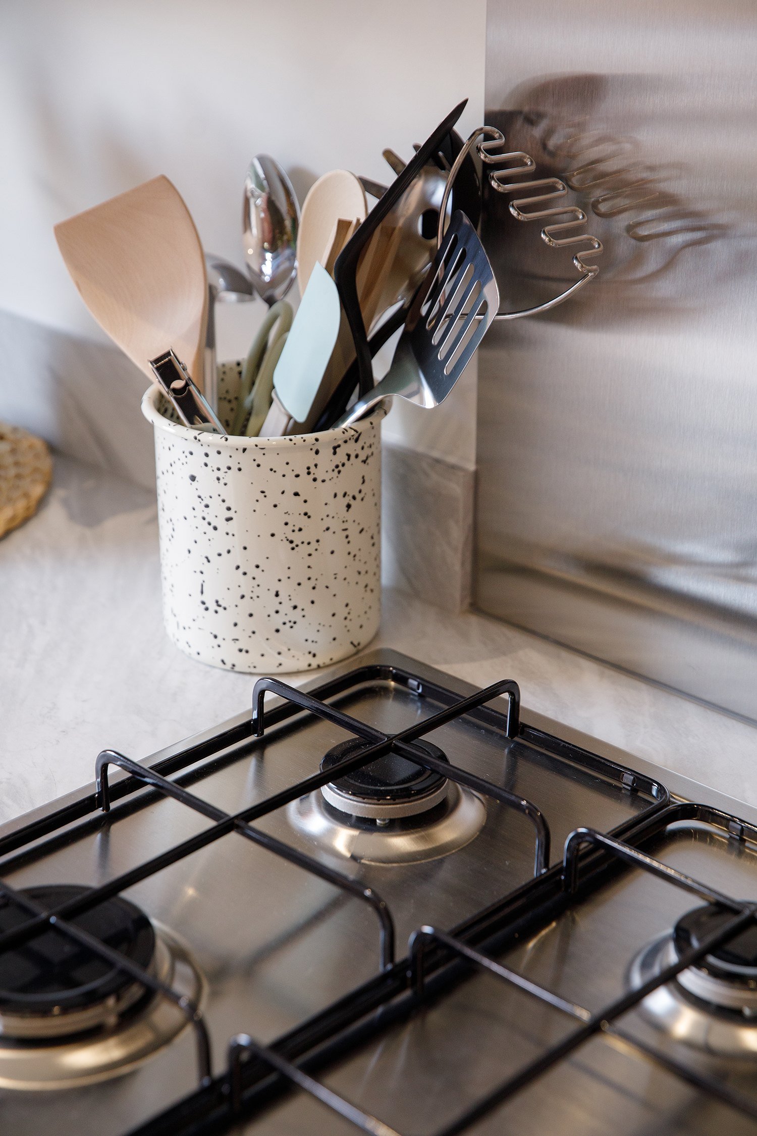 Kitchen stove with a speckled ceramic utensil holder filled with various kitchen utensils, including spatulas and spoons, next to a stainless steel backsplash.