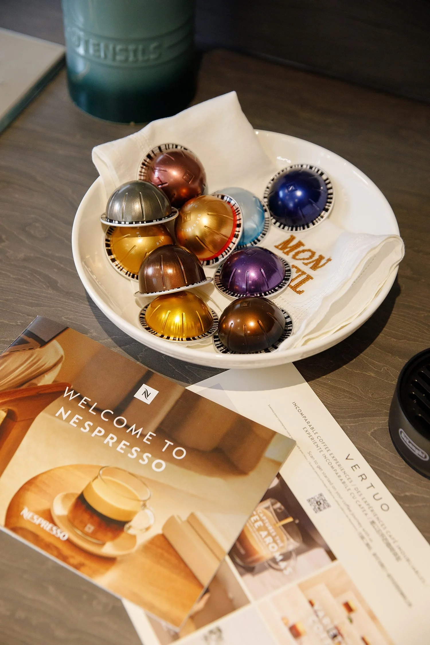 Colorful coffee capsules in a white bowl on a table next to Nestle coffee promotional materials and a Coffee Explorer brochure.