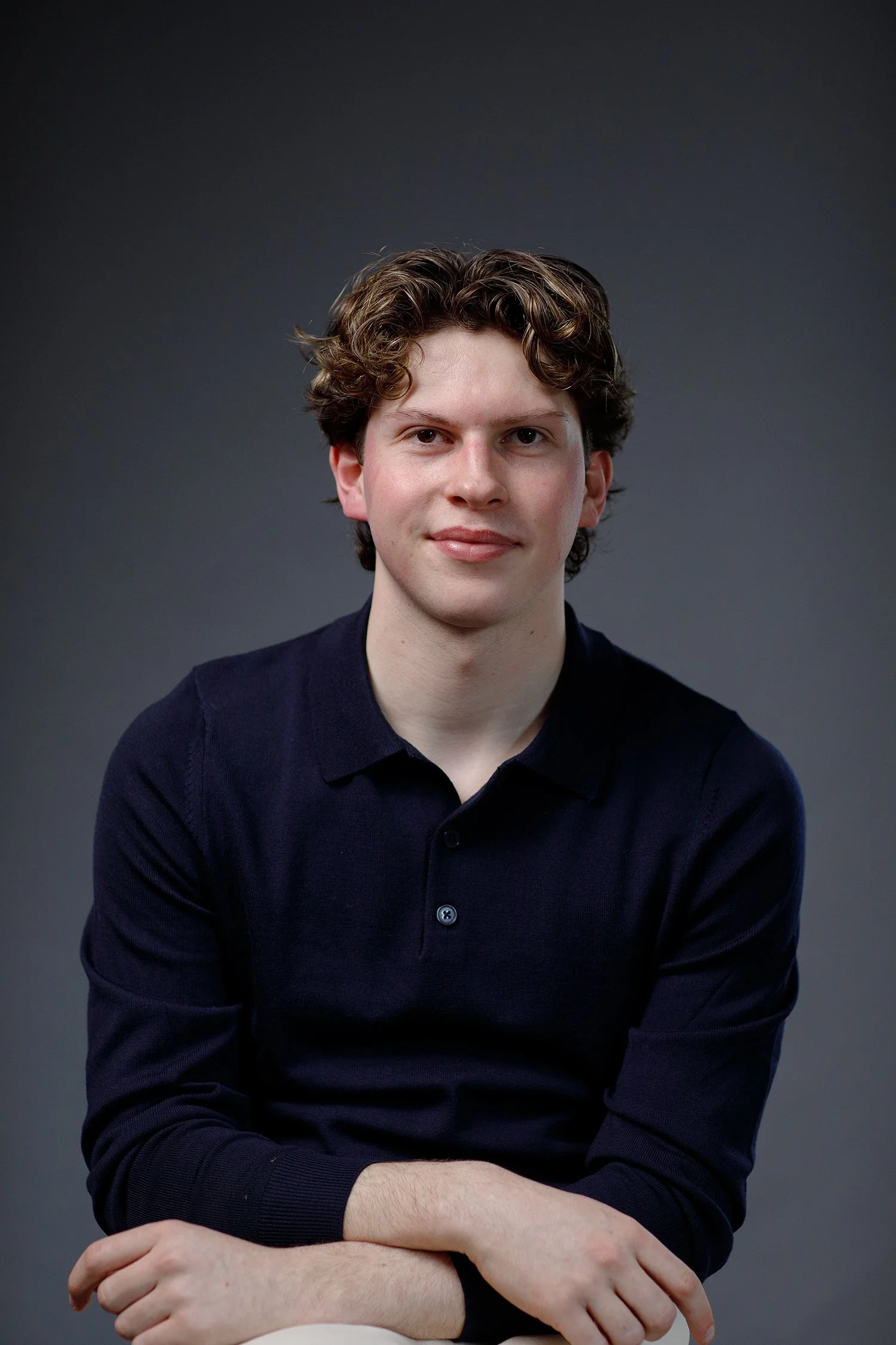 Portrait of Harvey Morson-Mills, wearing a dark navy sweater, sitting against a dark grey background.
