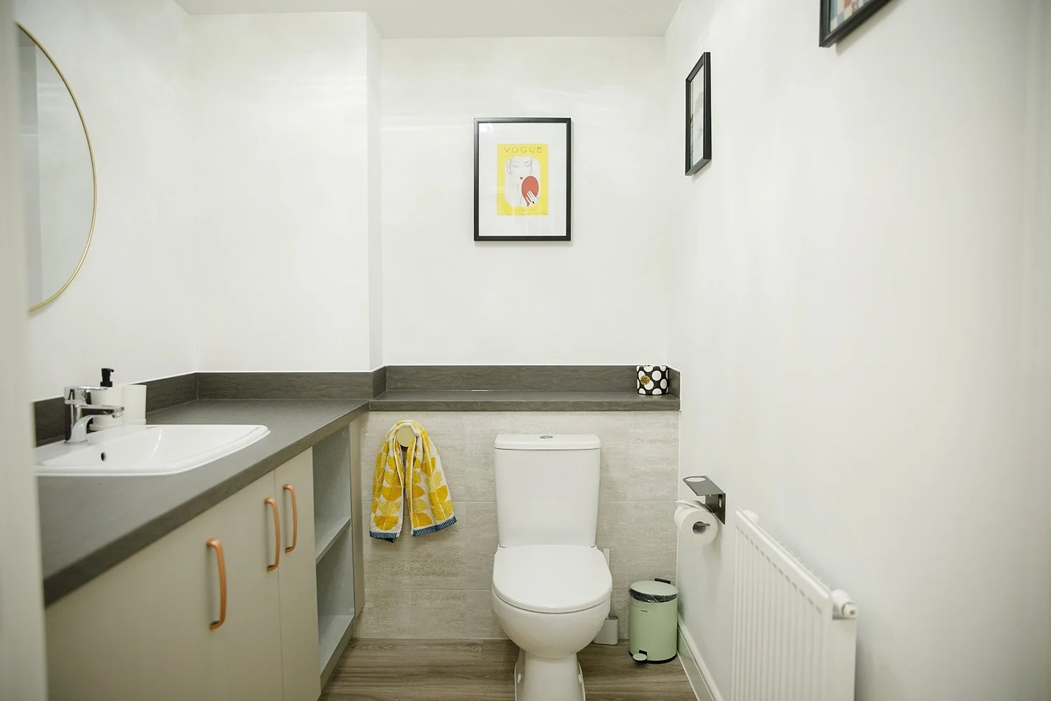 Simple modern bathroom with white walls, a toilet, gray counter with a sink, and framed artwork on the wall.