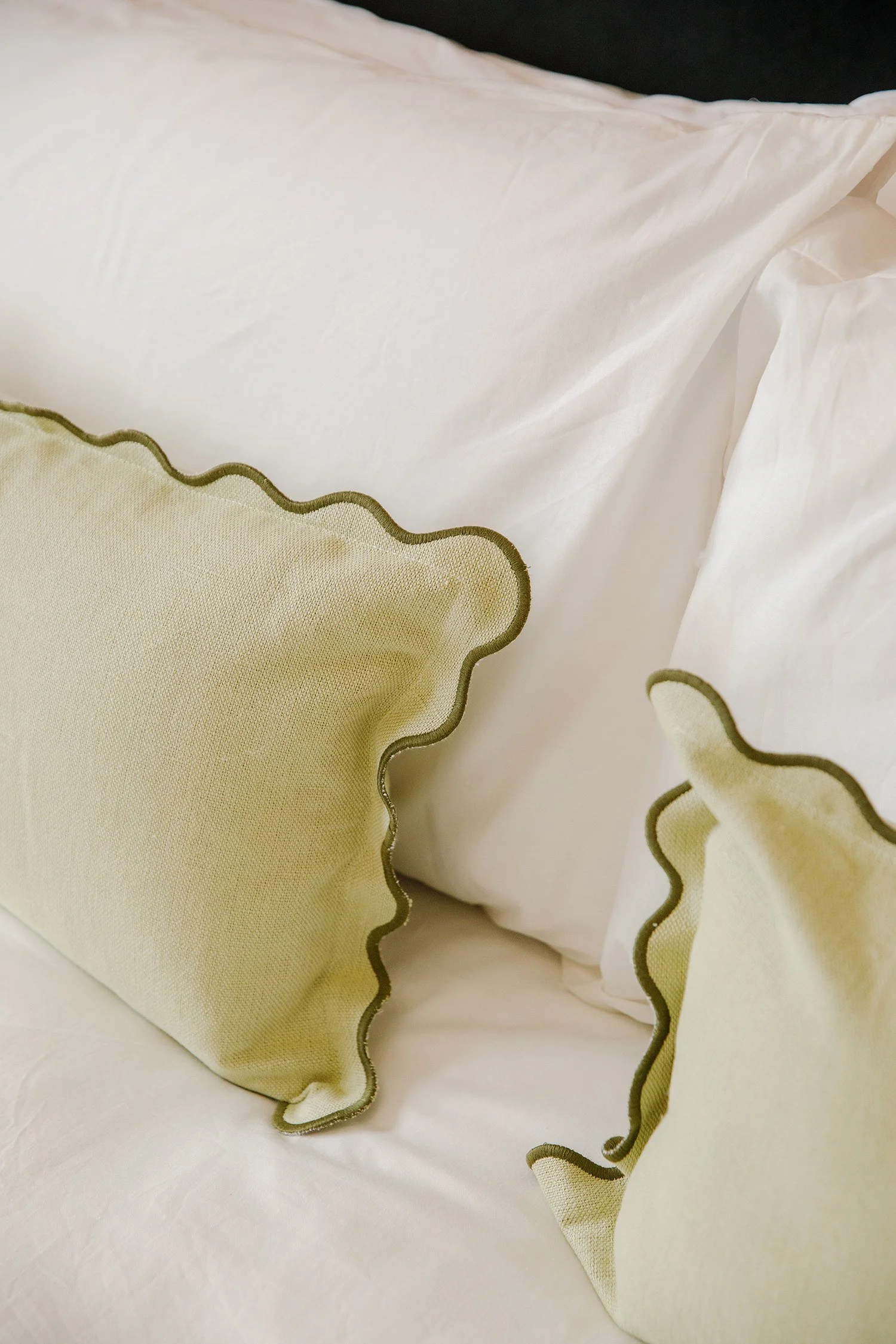 Close-up of a pastel yellow pillow with a ruffled edge and dark green piping on a white surface.