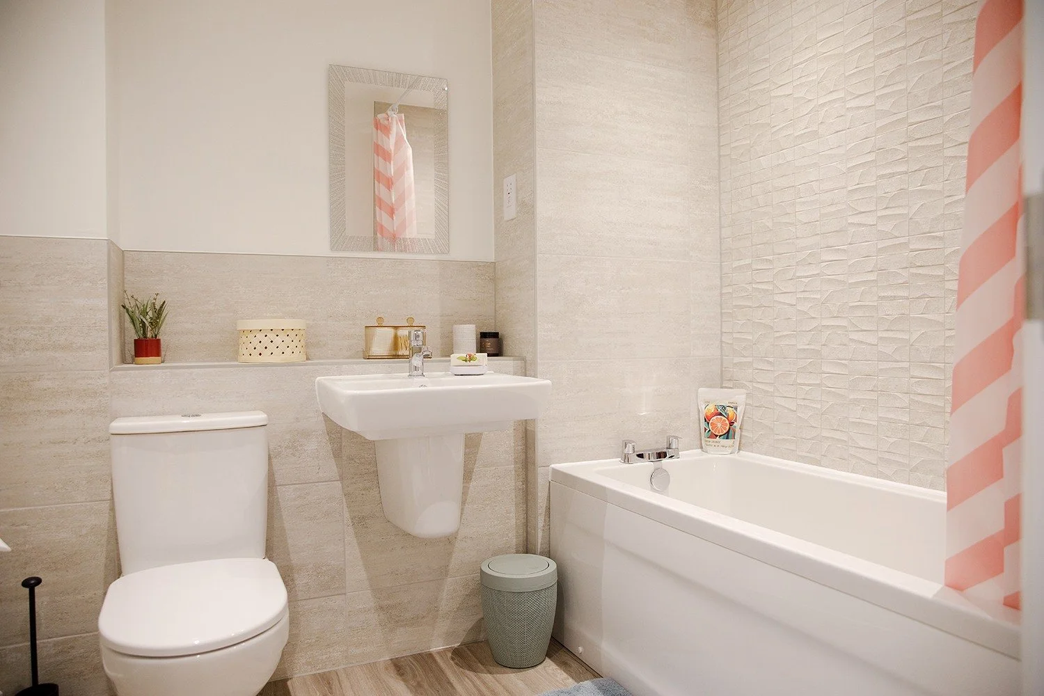 Bathroom with a white toilet, a small wall-mounted sink, a mirror, a potted plant, a decorative box, and a bathtub with a pink and white striped shower curtain.