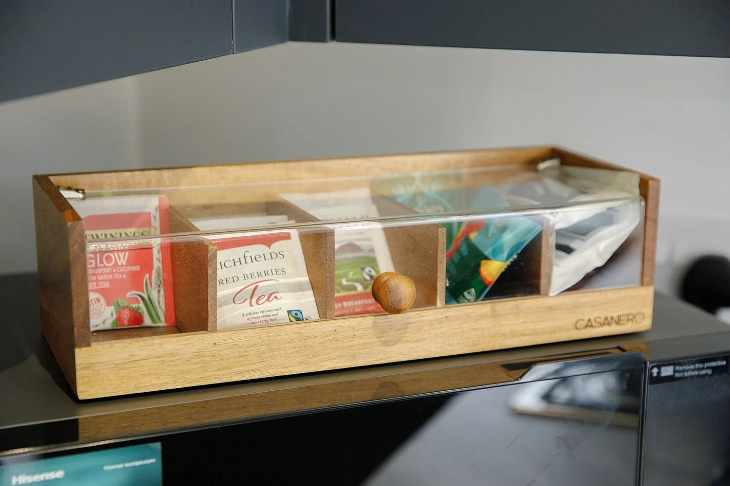 Wooden and glass tea storage box with various tea packets inside placed on a black surface.