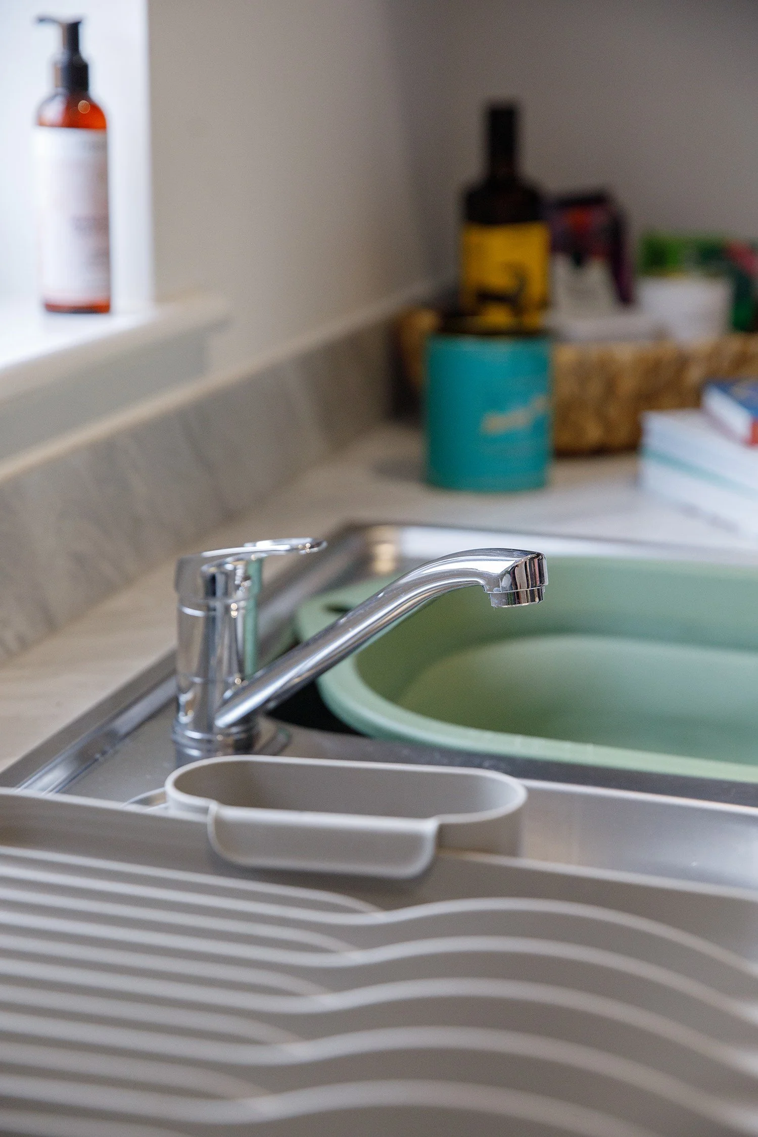 Kitchen sink with a faucet, dish rack, and cleaning supplies in the background.