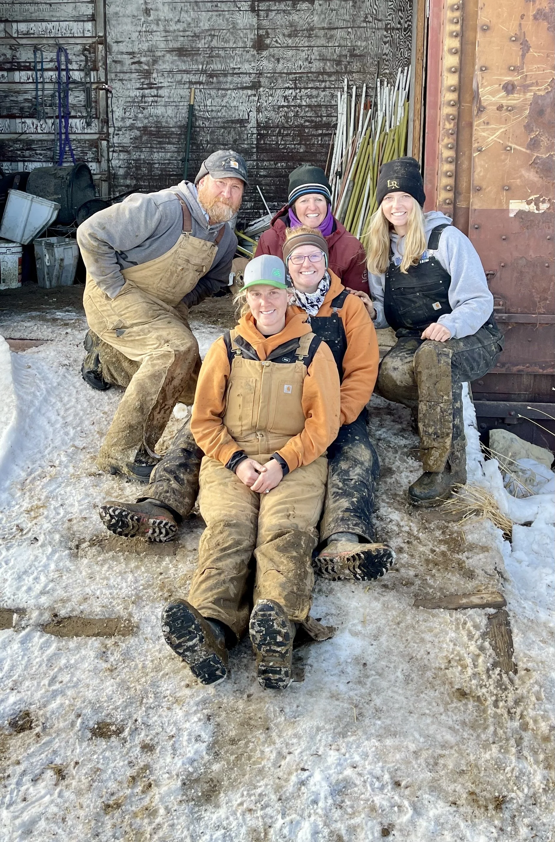 Five workers in outdoor snowy conditions, wearing work boots and clothing, posing for a group photo with smiles.