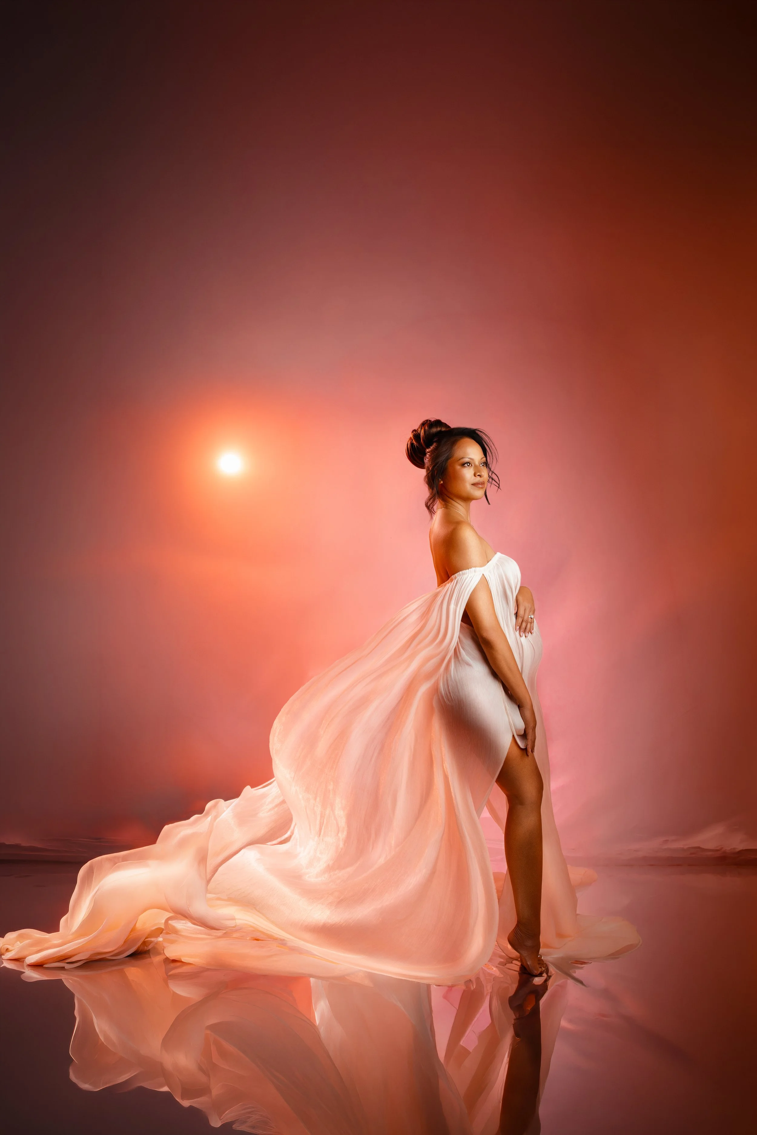 Luxury maternity portrait featuring a mother-to-be in a flowing white gown with warm sunset-inspired lighting at Esther Kay Studio in the San Francisco Bay Area.