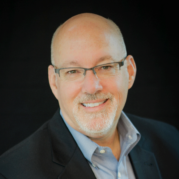 Headshot of a smiling middle-aged Caucasian man with glasses, a light blue shirt, and a dark blazer, against a black background.