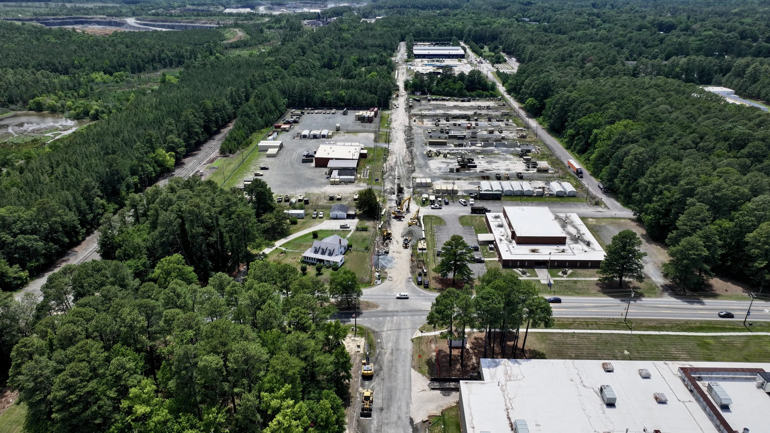 Aerial view of a construction site and surrounding greenery, with buildings, trees, and vehicles.