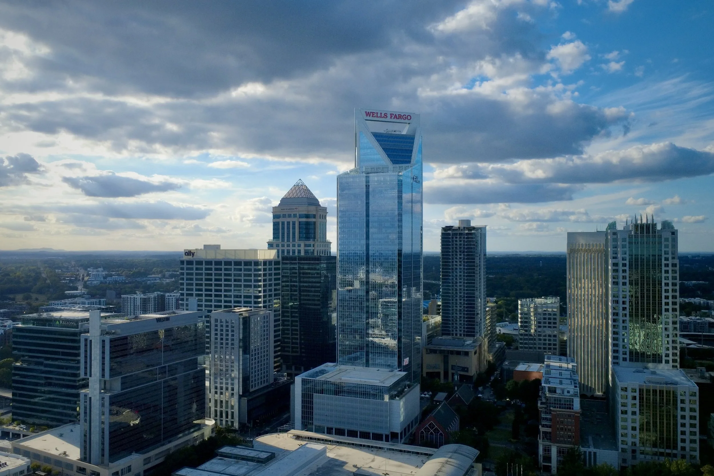 Skyscrapers in a city skyline, with a prominent glass building bearing the Wells Fargo logo under a cloudy sky.