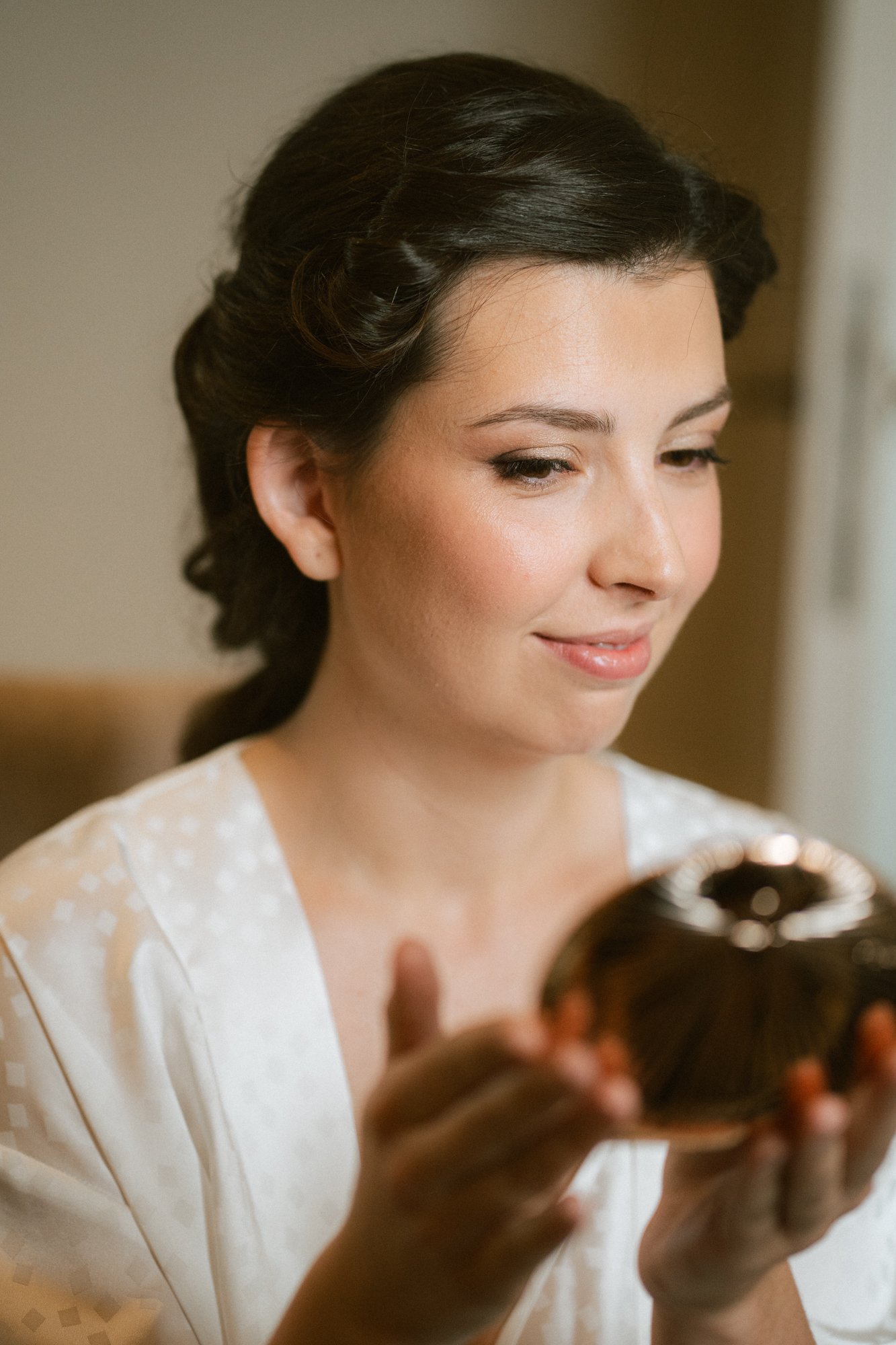 Mujer con maquillaje y cabello peinado, sosteniendo y mirando un objeto decorativo de color negro con detalles dorados.