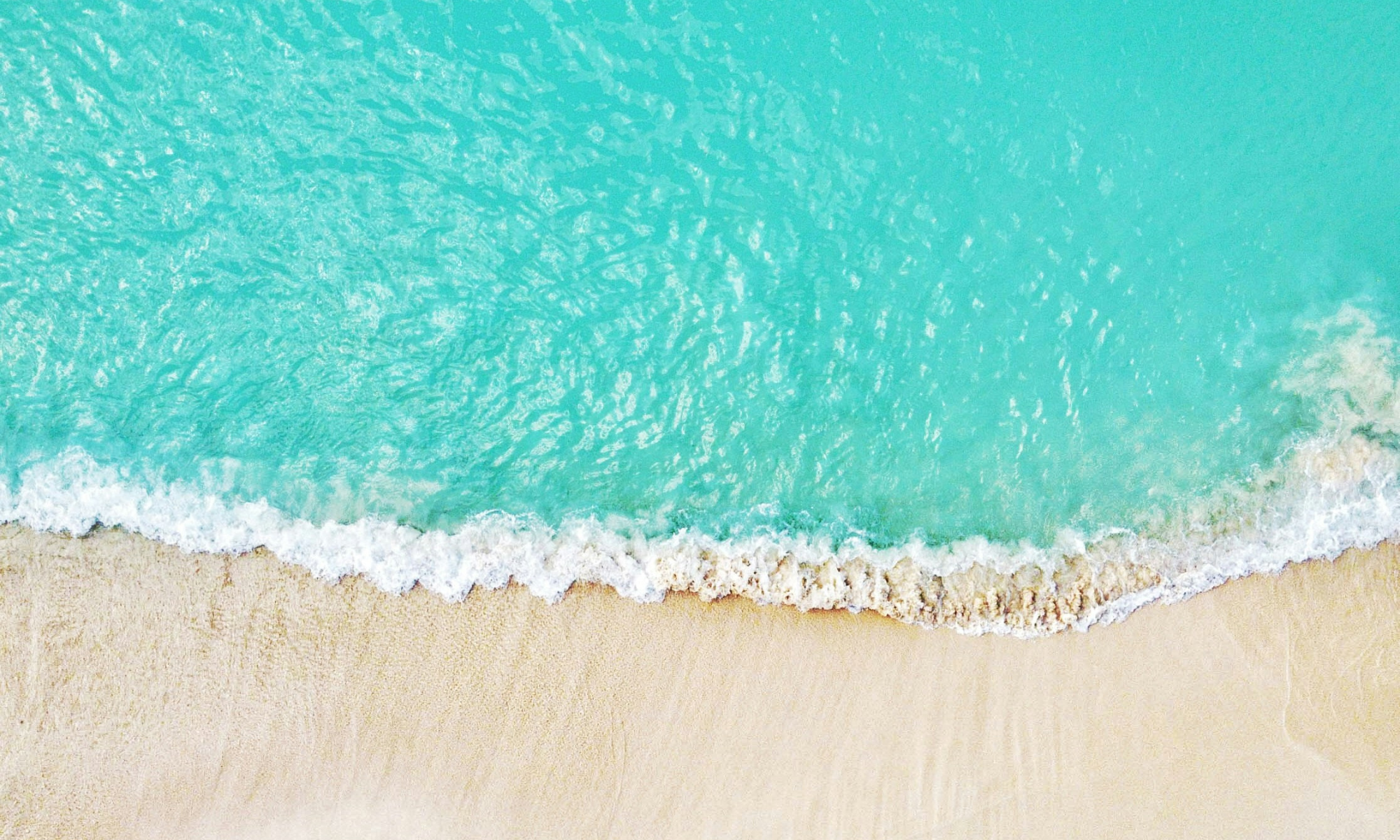 Turqoise ocean meets shoreline with sandy beach