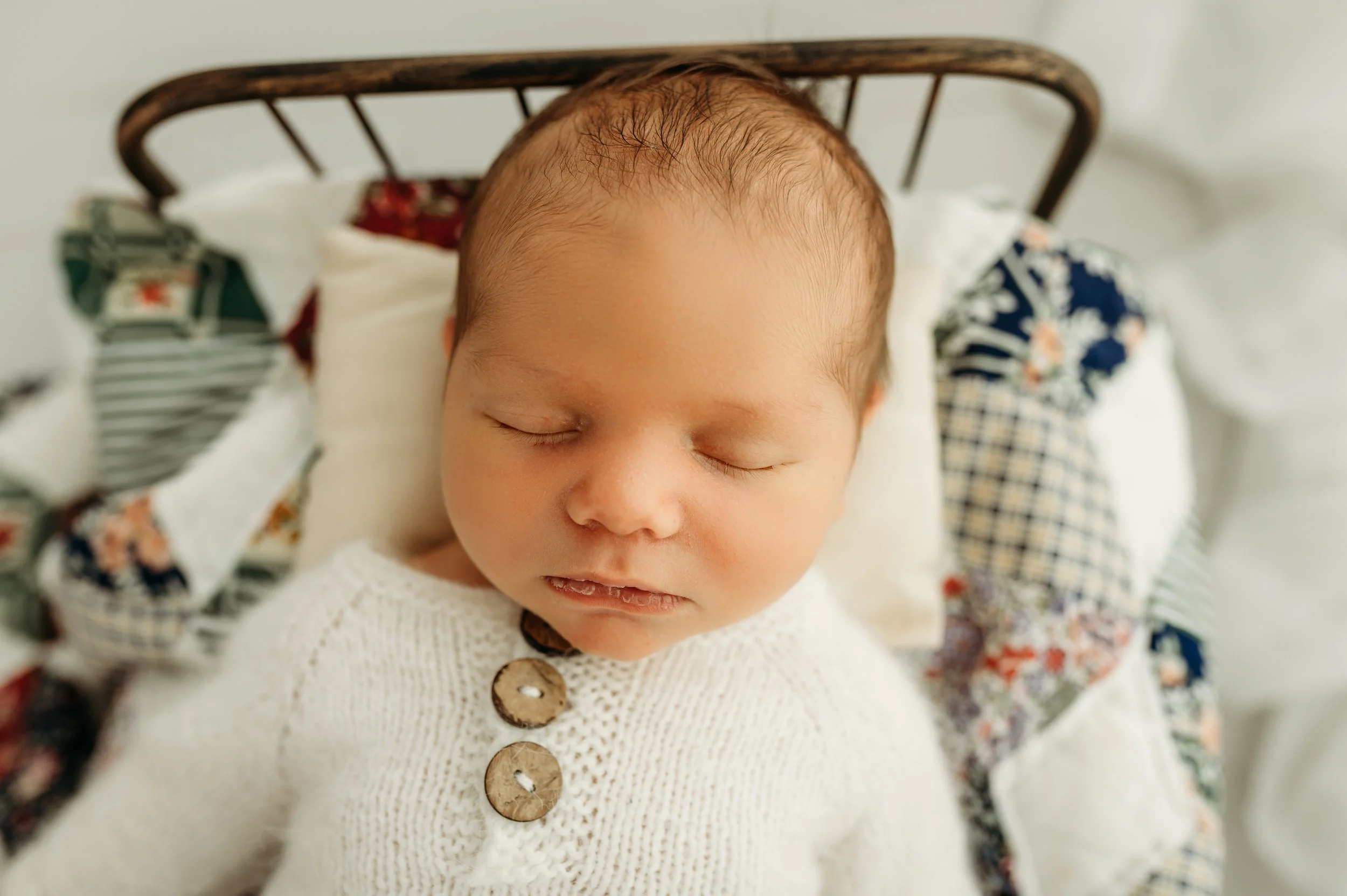 newborn baby boy in a bed with a beautiful quilt sleeping in a clarksville tn newborn photography studio