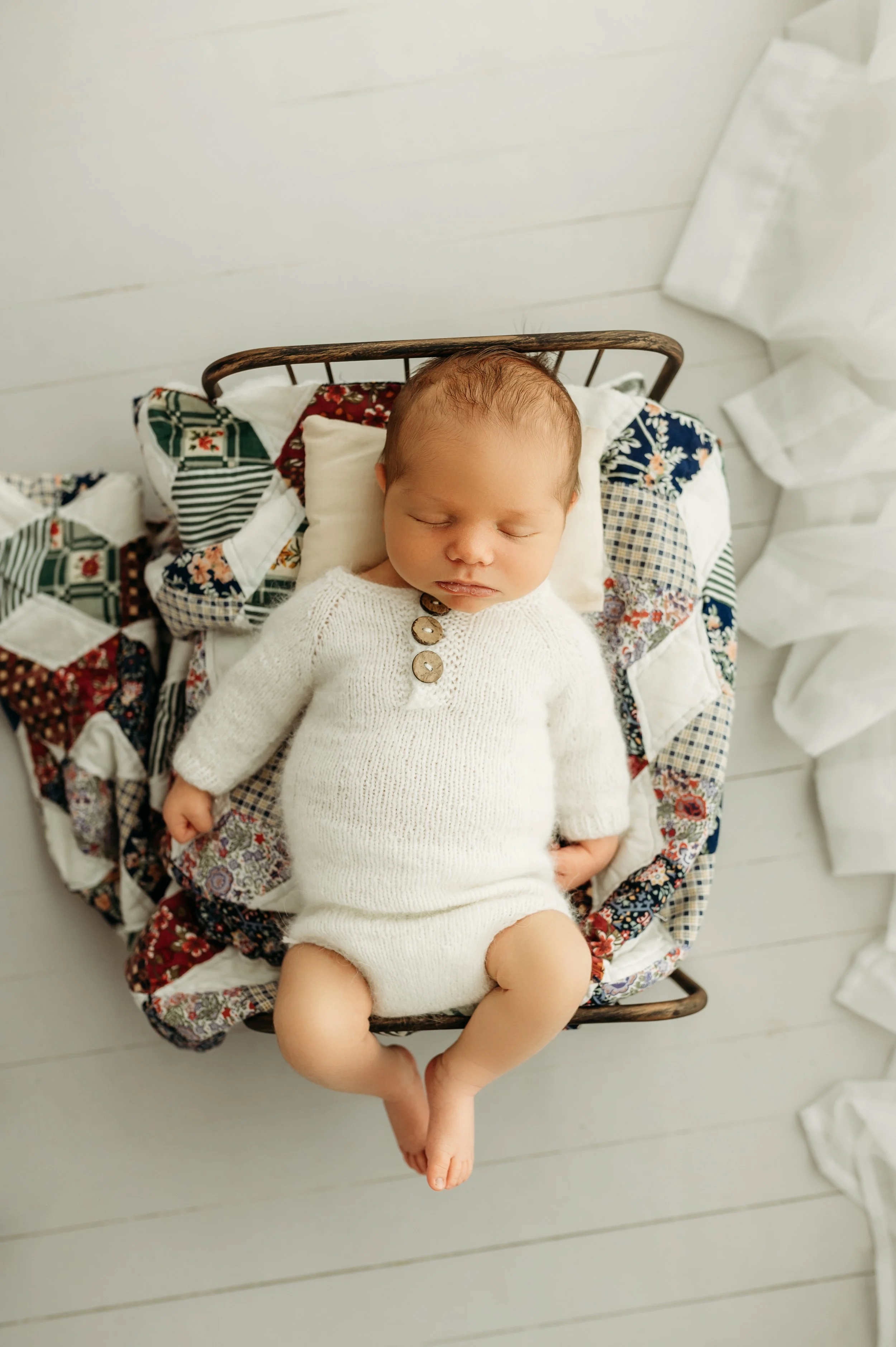 newborn baby boy on a tiny bed with a stunning quilt by a clarksville, tn newborn photographer