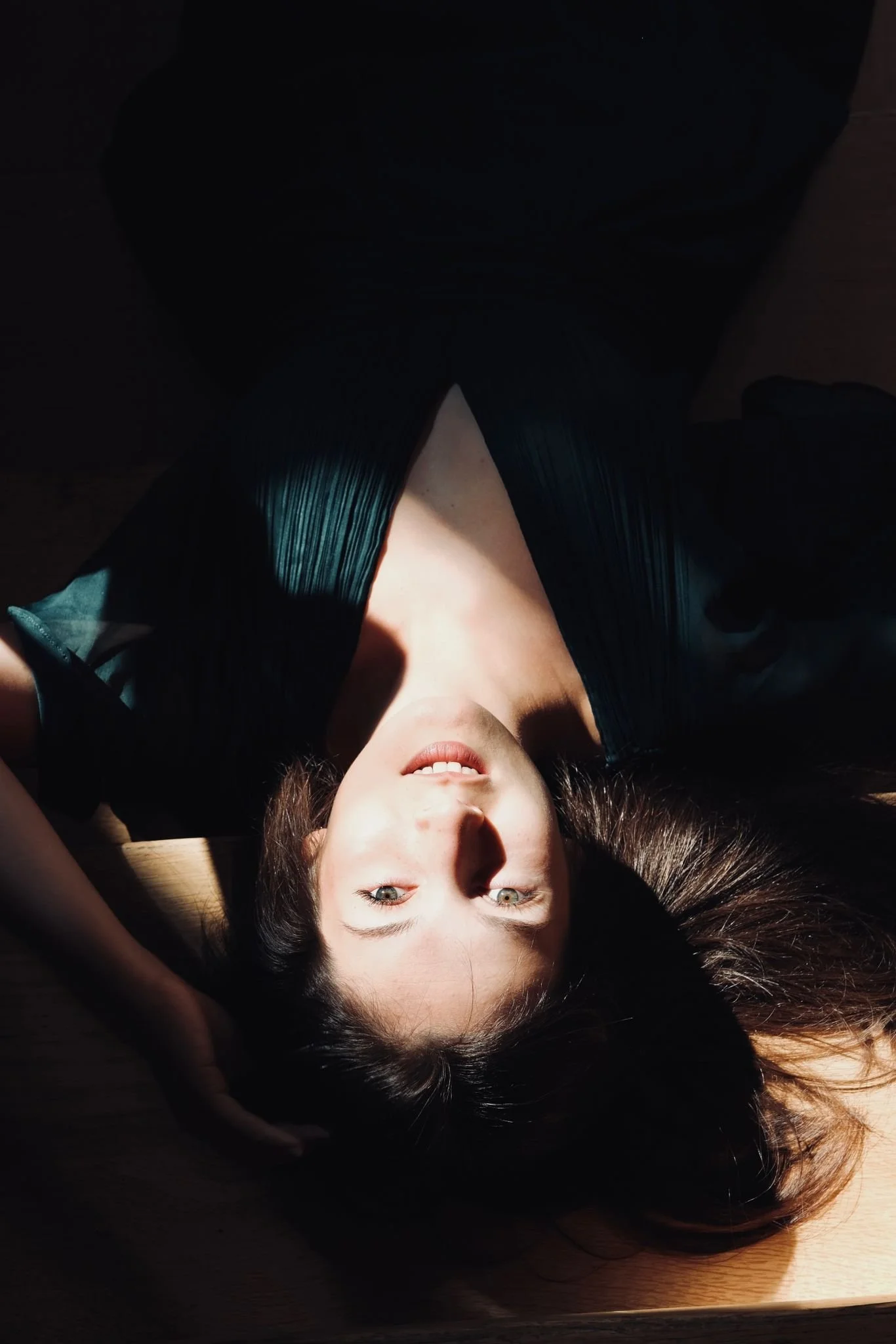 Frau liegt auf dem Rücken, im Sonnenlicht, mit dunkler Kleidung und offenen Haaren.