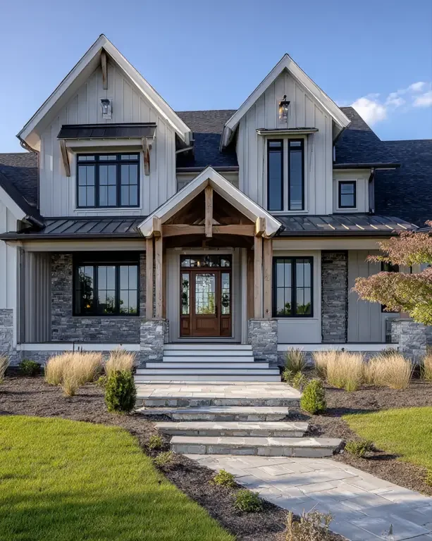 Front view of a modern two-story house with stone and siding exterior, multiple gabled roofs, and a wooden front door, surrounded by a landscaped yard with grass, shrubs, and trees.