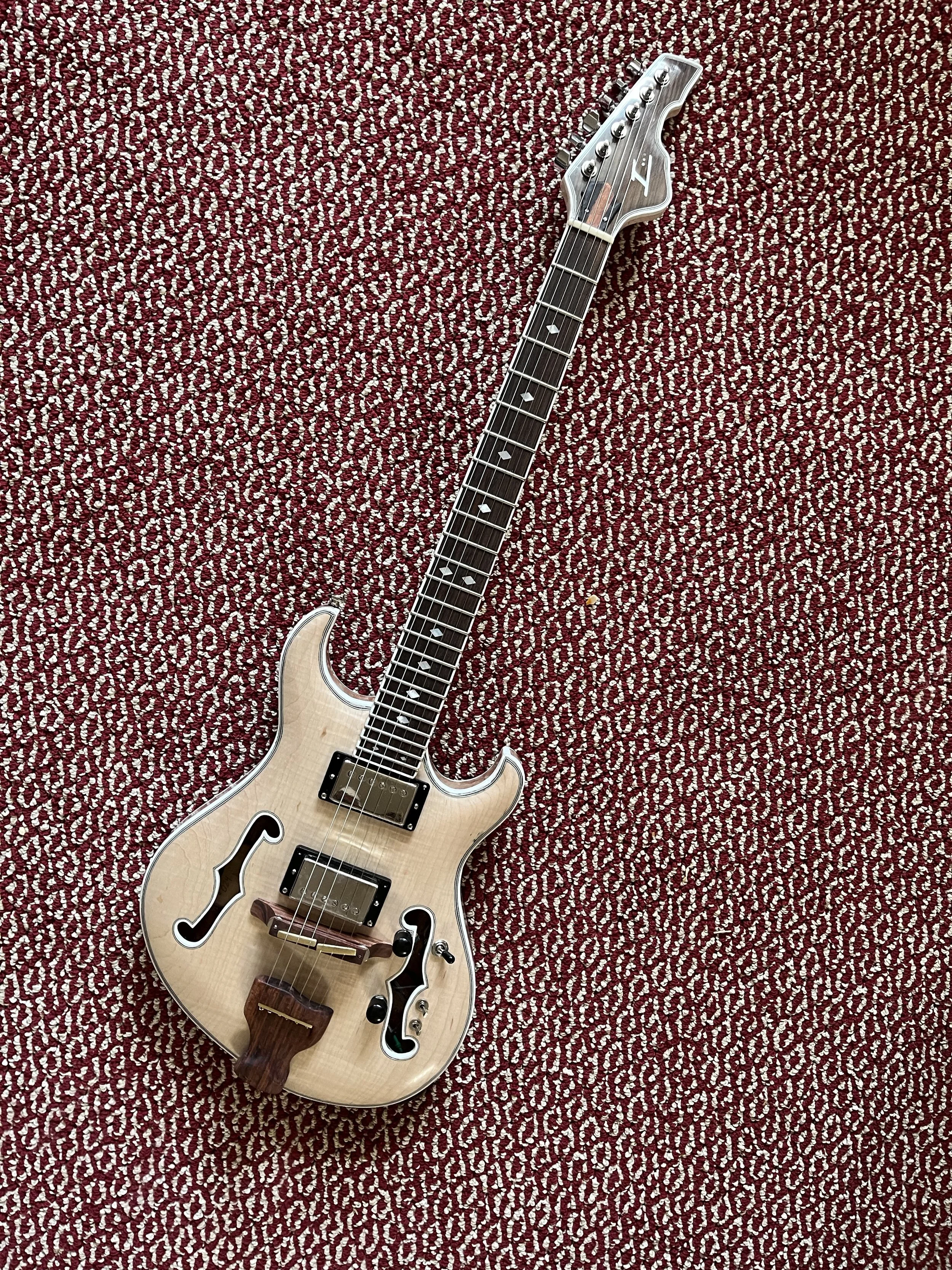 A cream-colored electric guitar lying on a red and white patterned carpet.