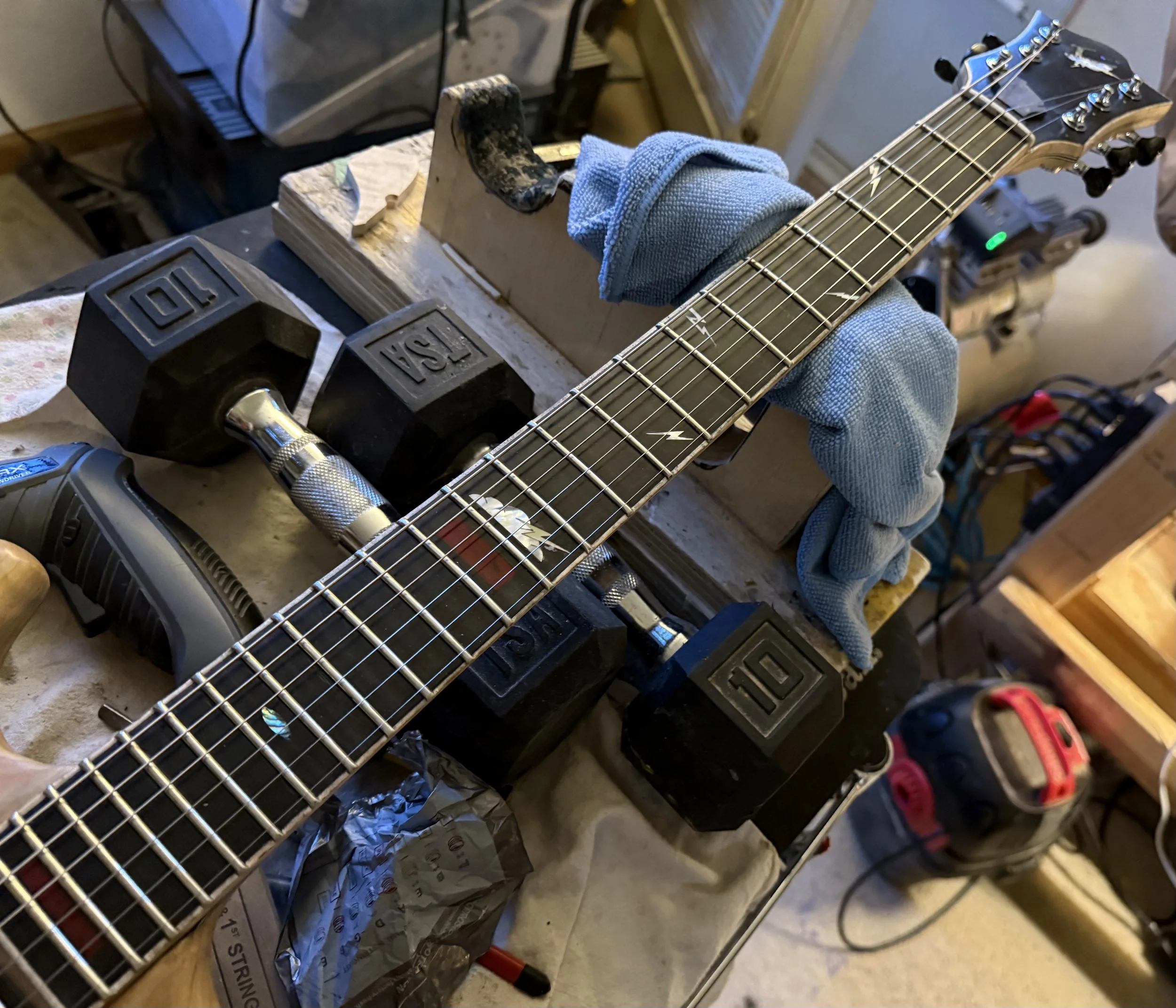 A guitar clamped in a workbench with a blue cloth on the neck, surrounded by tools and equipment in a workshop.