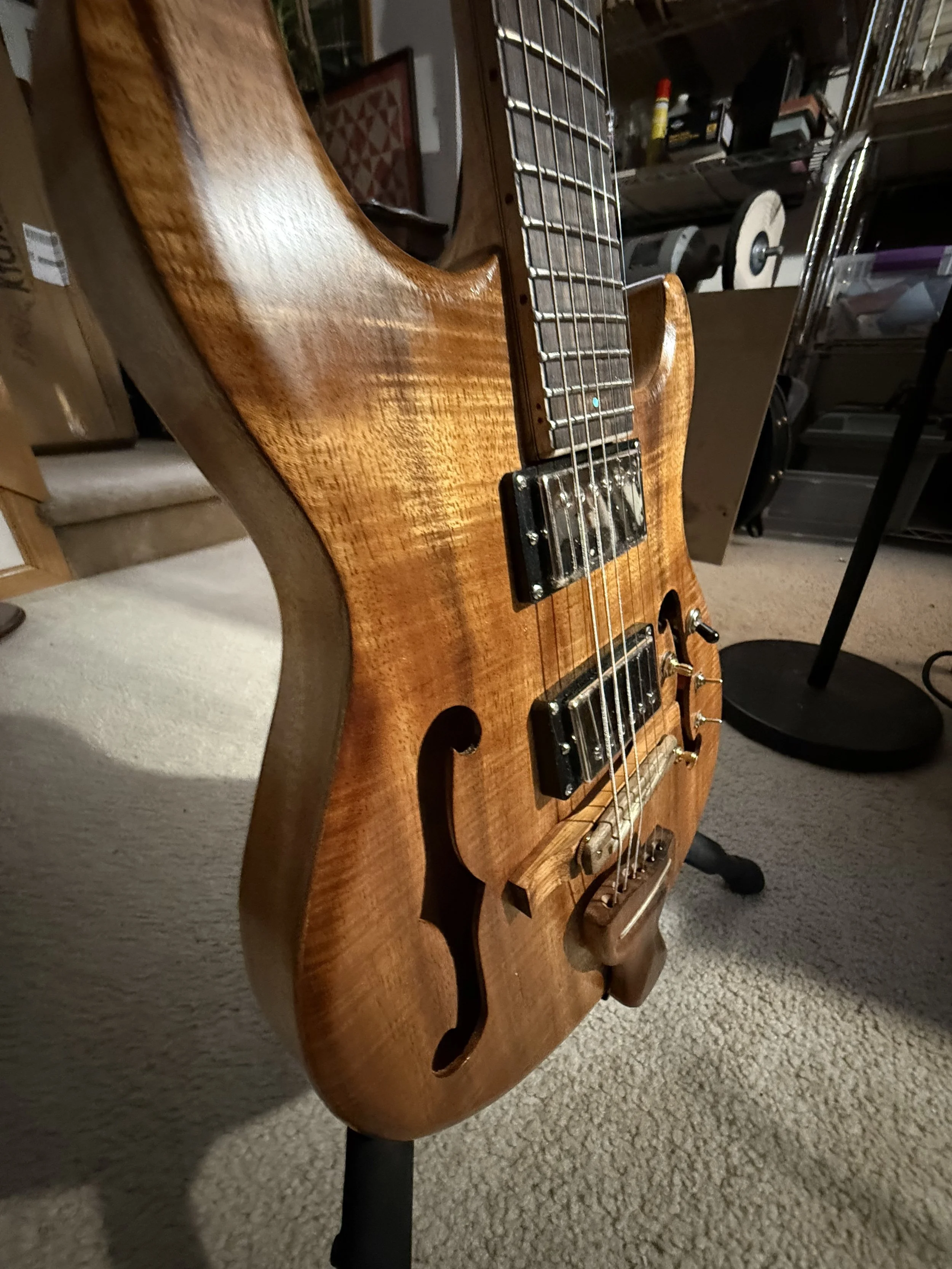 A wooden electric guitar on a black stand in a room with shelves and storage containers.