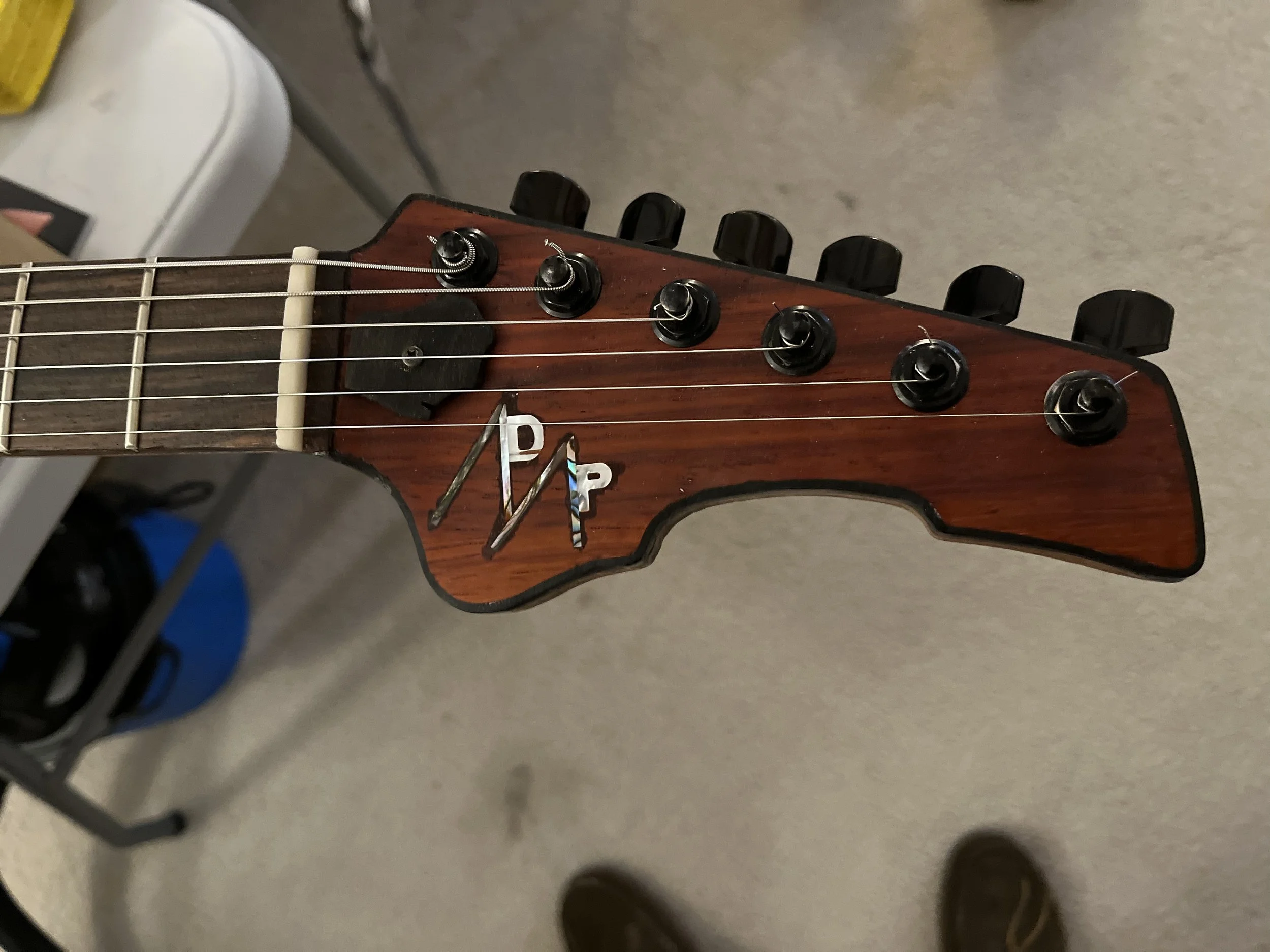Close-up of an acoustic guitar's headstock with tuning pegs and strings, seen from an overhead perspective against a gray background.