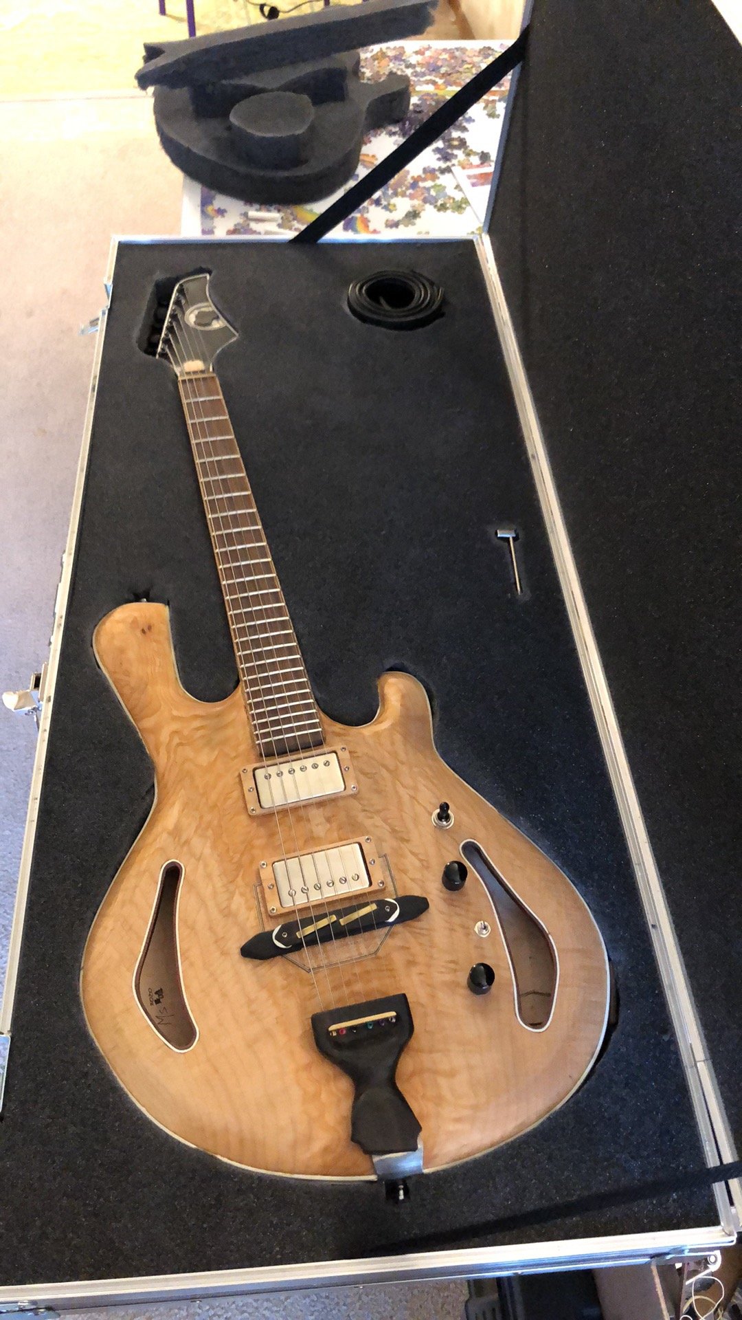 Electric guitar with a natural wood finish inside a hard case with black foam lining.