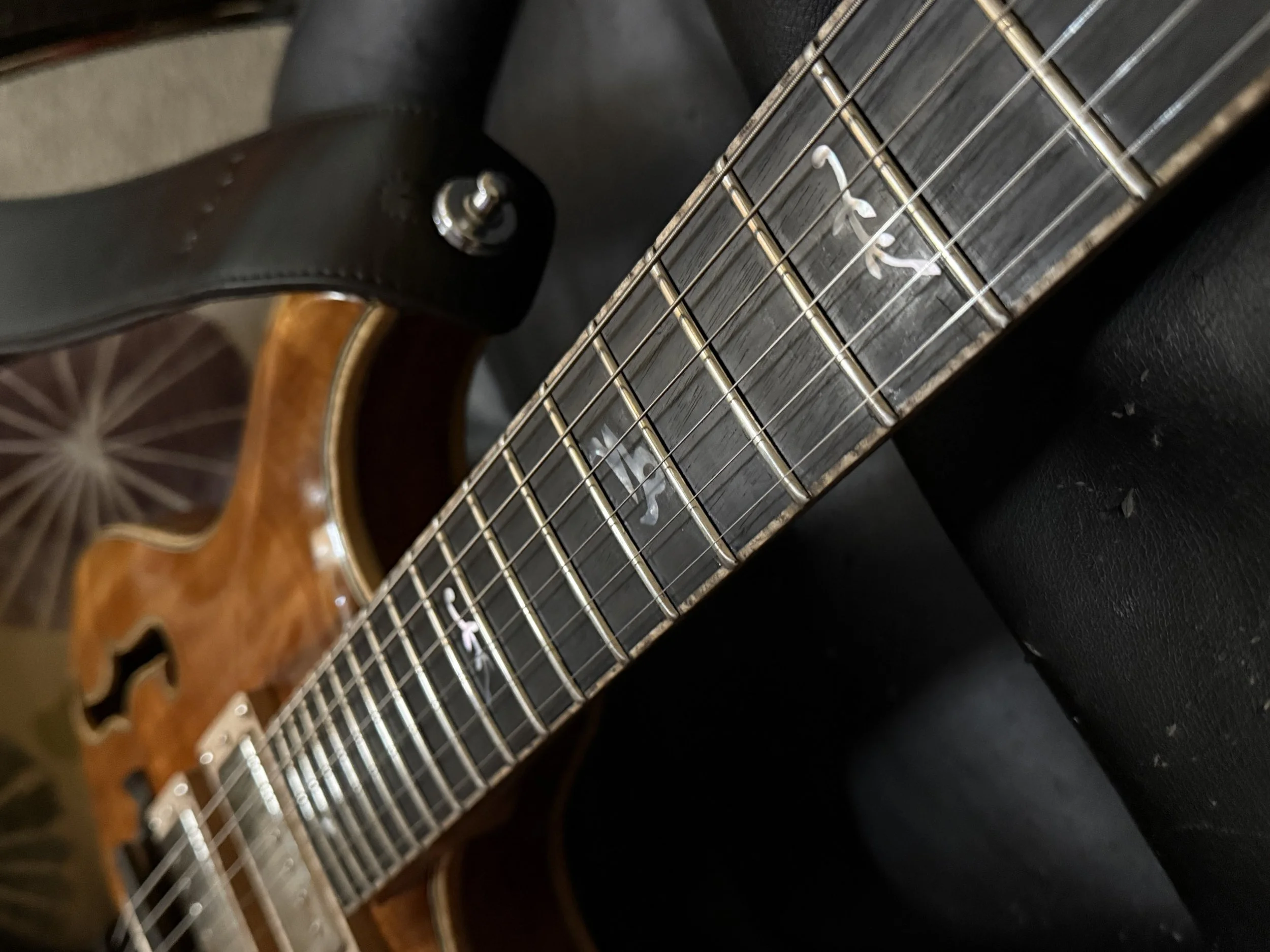 Close-up view of an electric guitar, showing its neck, fretboard, and strings, with a black body and a decorative inlay on the fretboard.