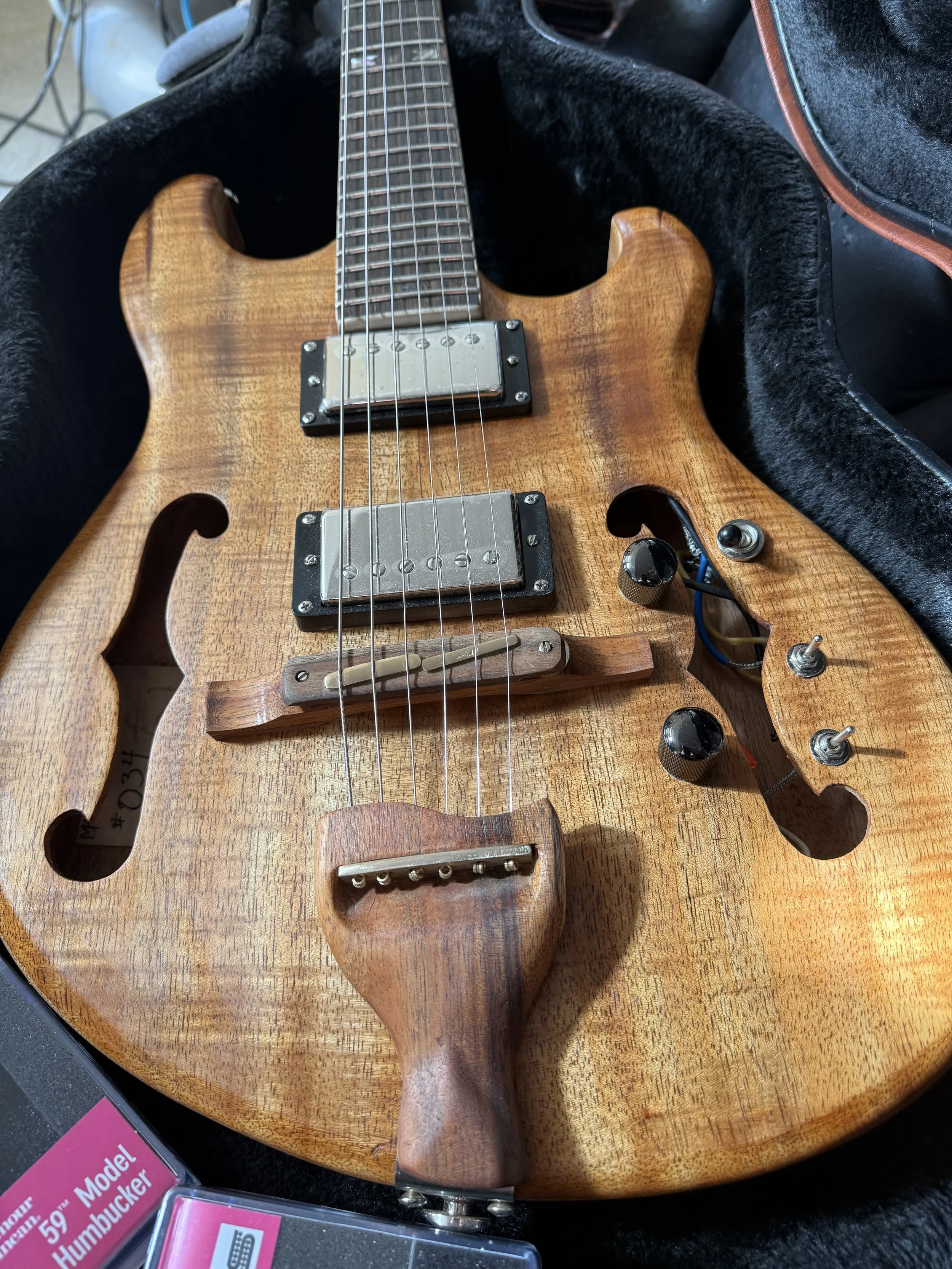 Close-up view of a vintage electric guitar with a natural wood finish, resting inside a black plush-lined case.