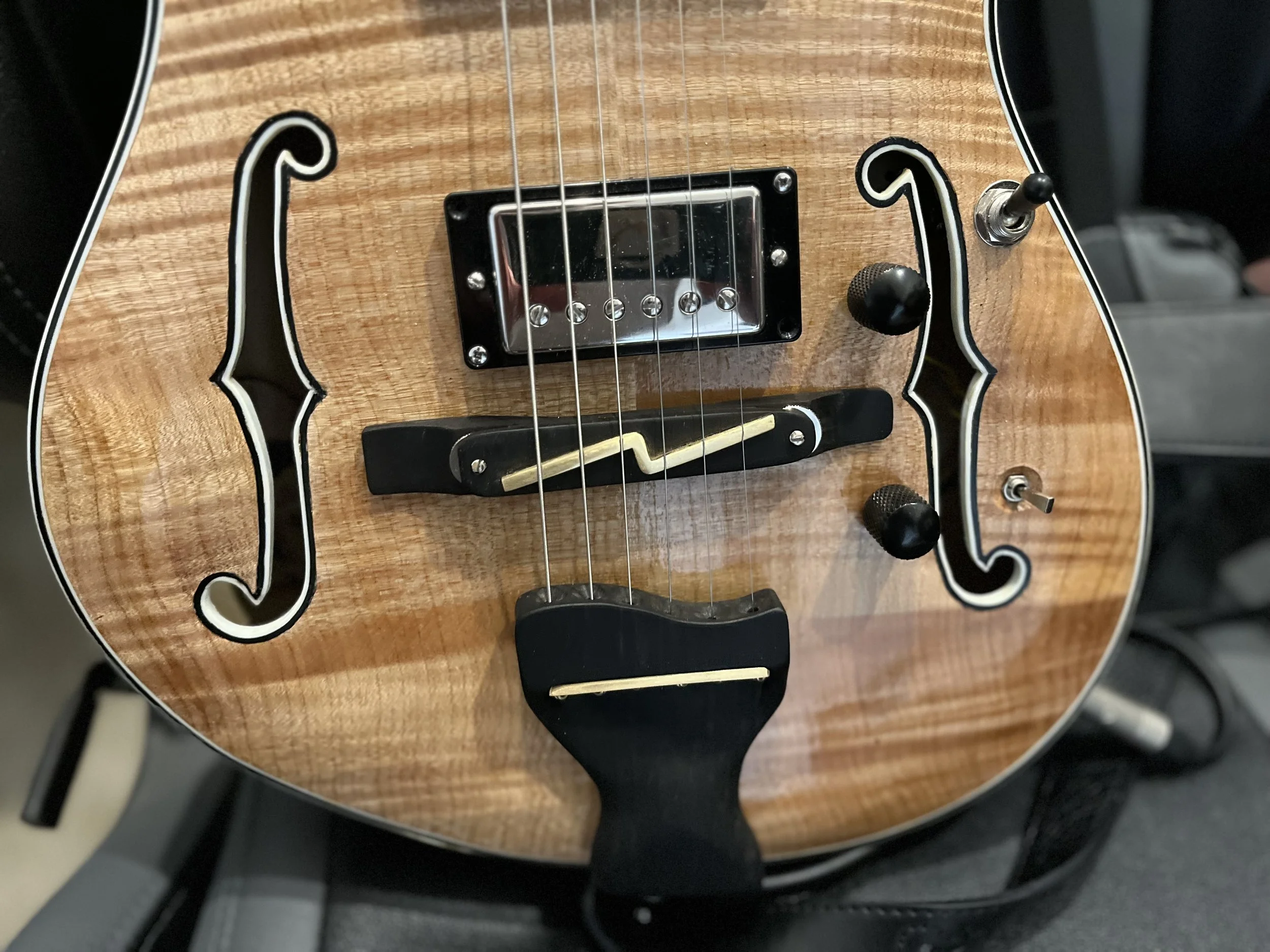 Close-up of an electric guitar with a natural wood finish, black and white detailing, a single pickup, and control knobs.